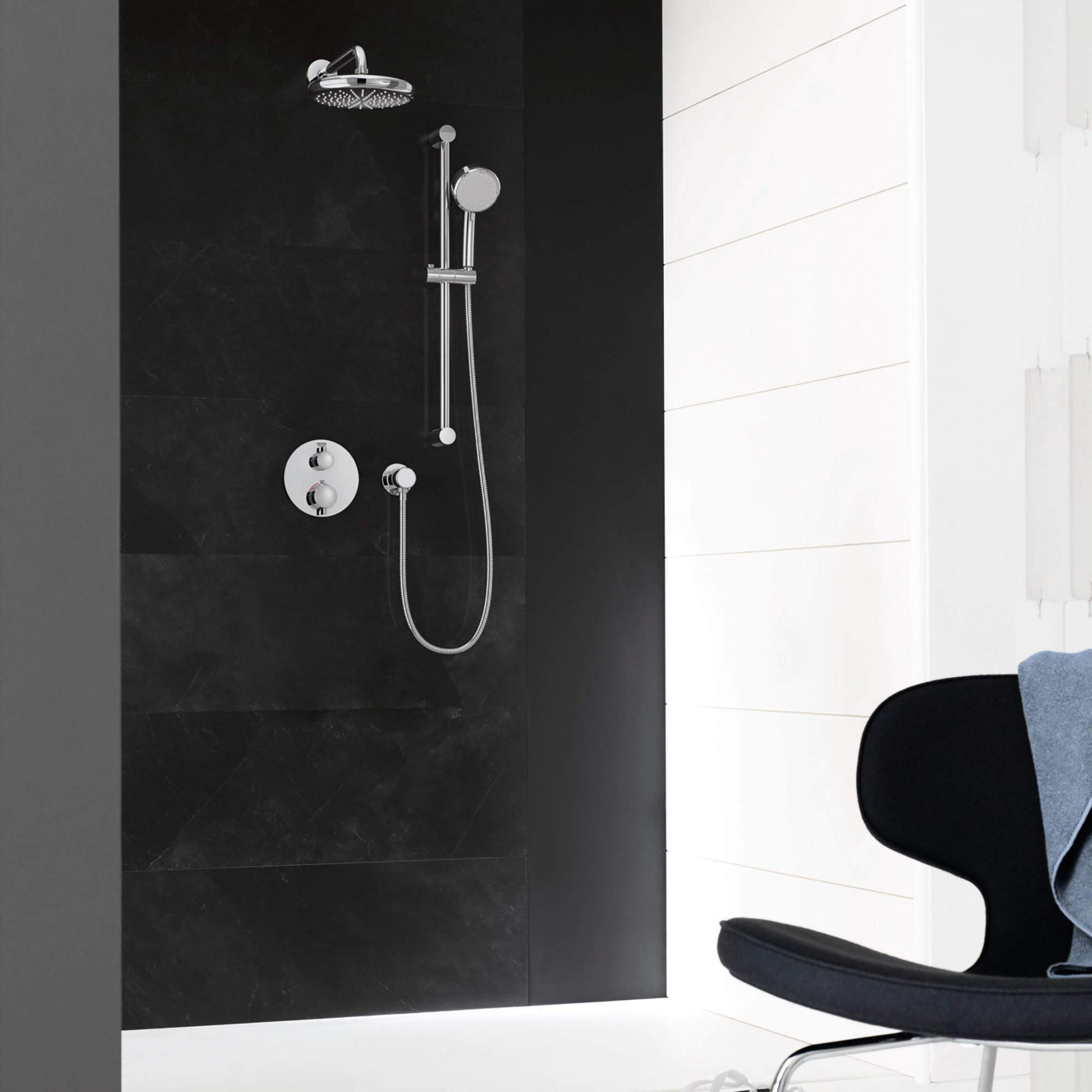Chrome shower system mounted on dark tile wall with overhead rainfall showerhead, handheld shower, vertical rail, and round c