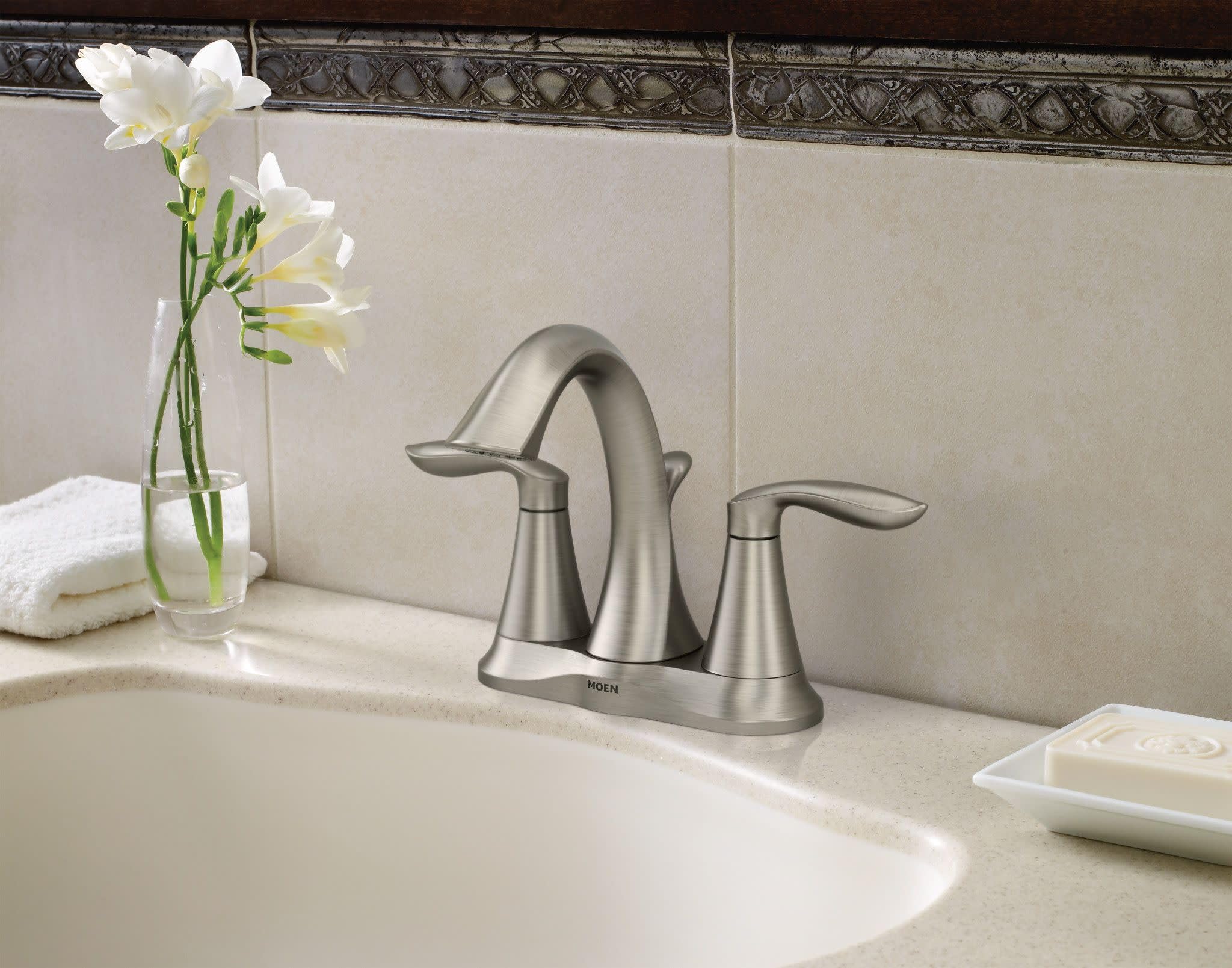 Brushed nickel two-handle bathroom faucet with curved spout installed on white sink countertop.