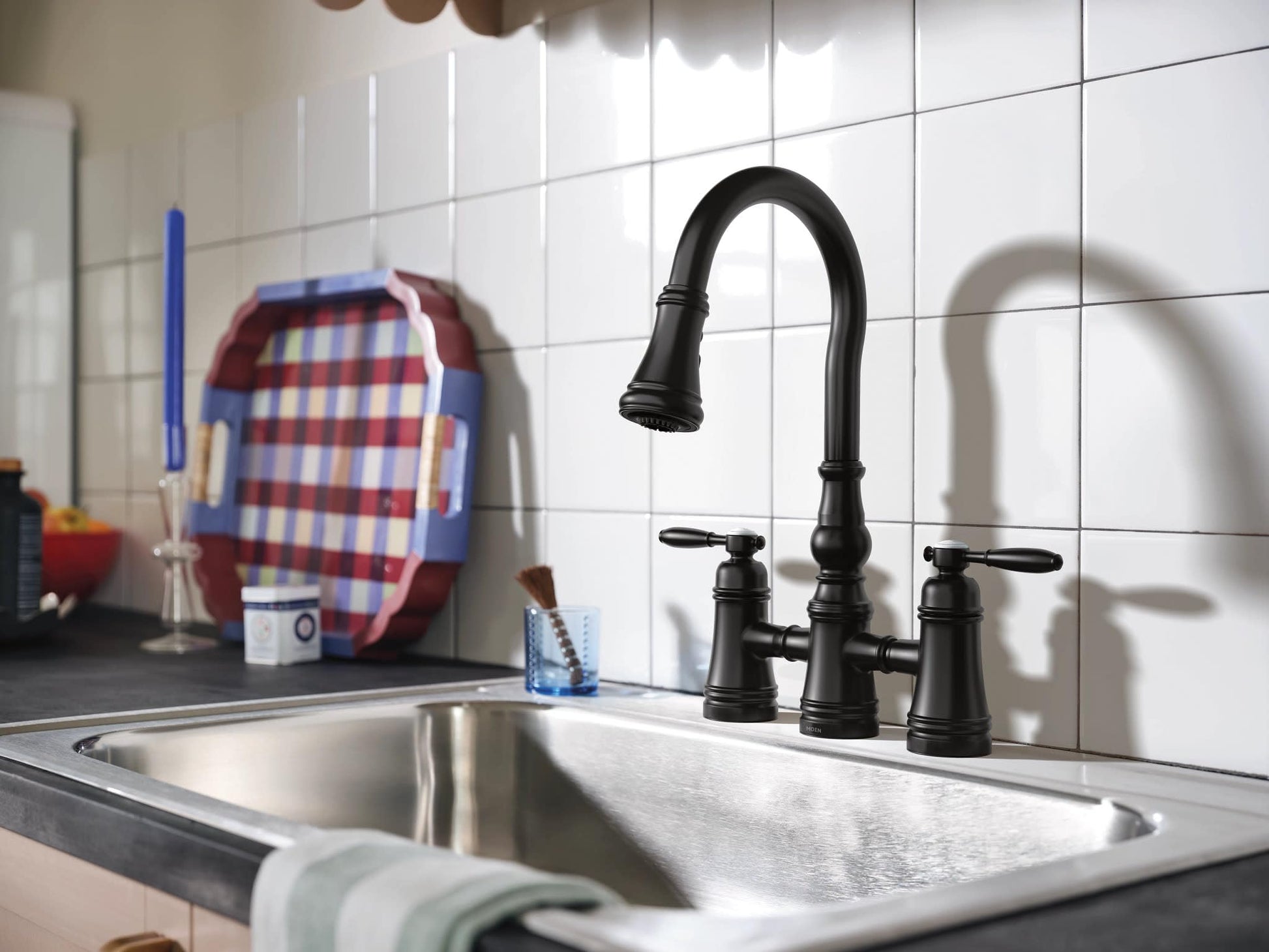 Matte black two-handle bridge kitchen faucet with pulldown sprayer and curved spout over stainless steel sink.
