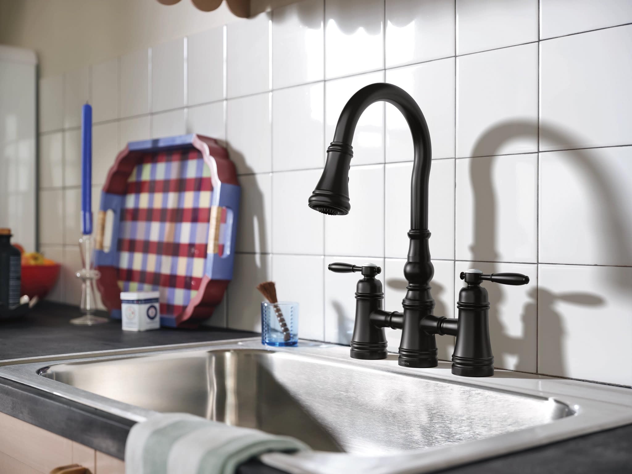 Matte black two-handle bridge kitchen faucet with pulldown sprayer and curved spout over stainless steel sink.