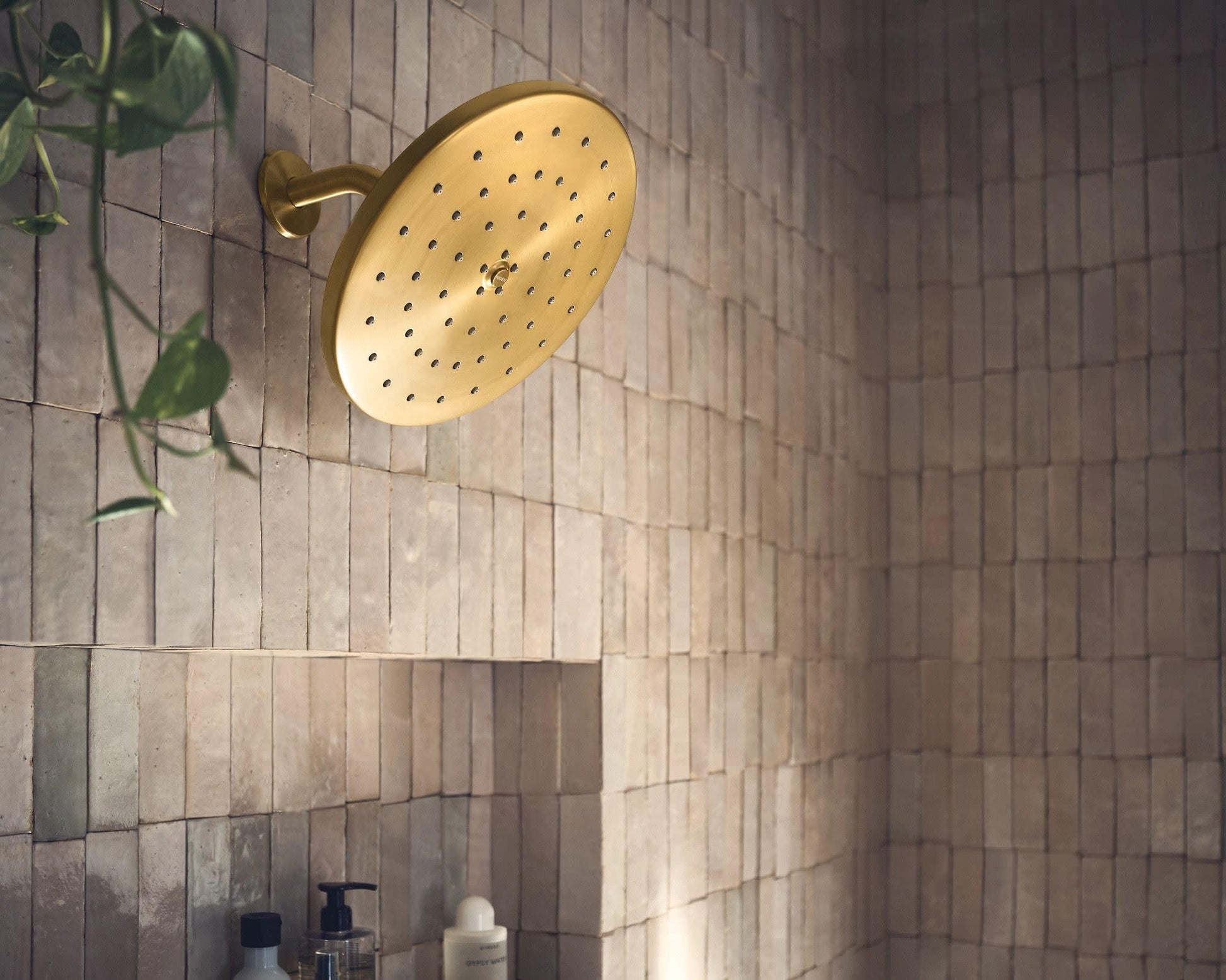 Brushed gold round shower head with multiple spray holes mounted on tile wall.