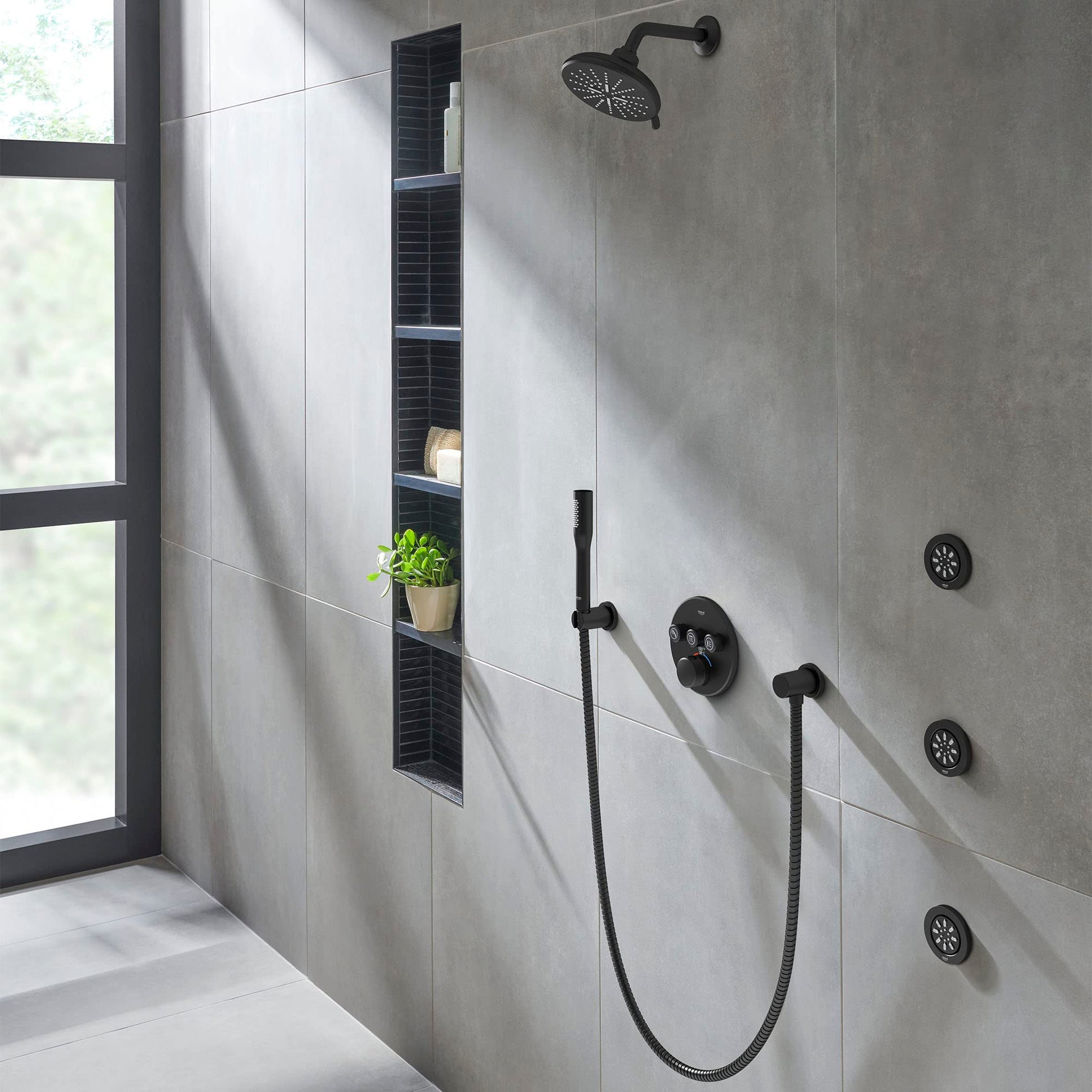 Matte black thermostatic valve trim with overhead rain showerhead, handheld sprayer, and body jets installed in shower wall.