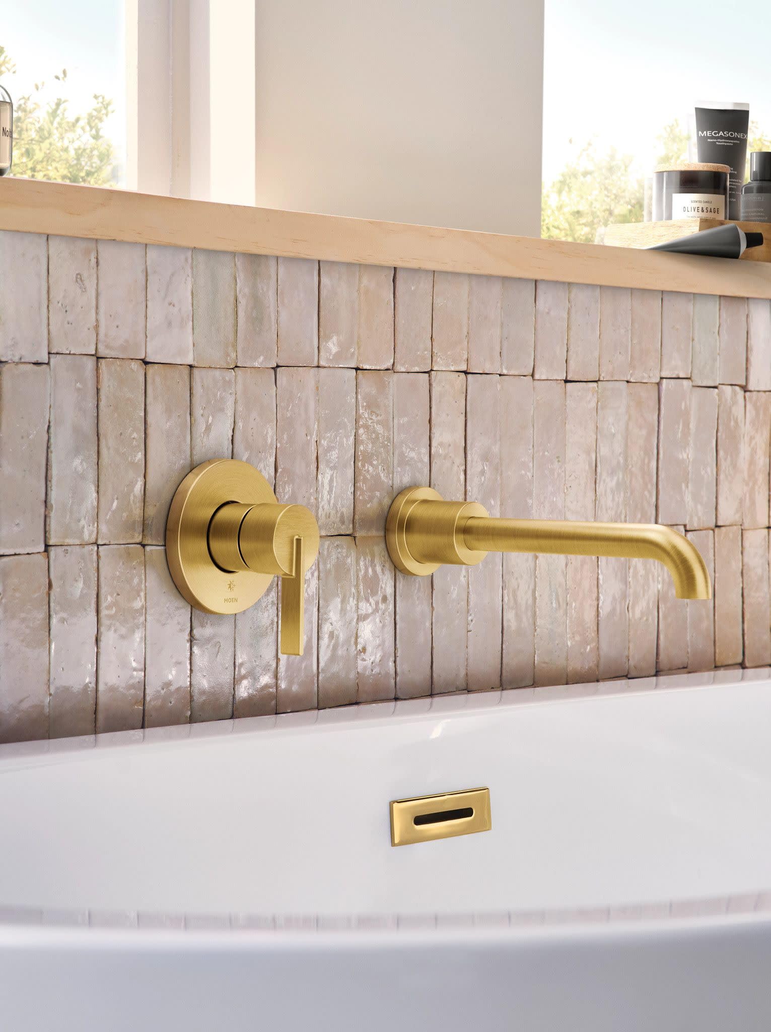 Brushed gold wall-mounted tub faucet with single lever handle and curved spout installed above white soaking tub.