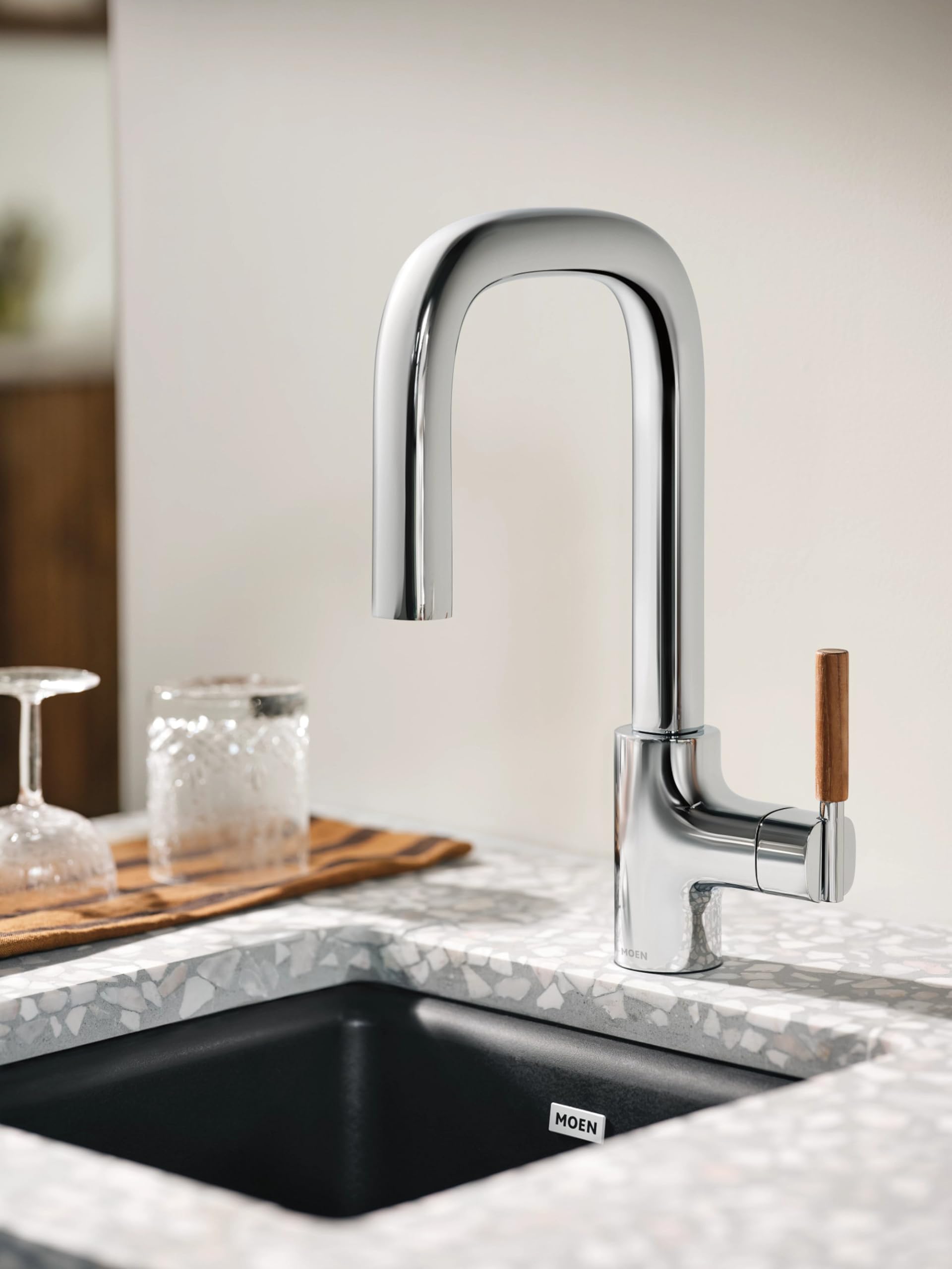 Chrome pulldown kitchen faucet with single lever handle and wooden accent installed above black sink.