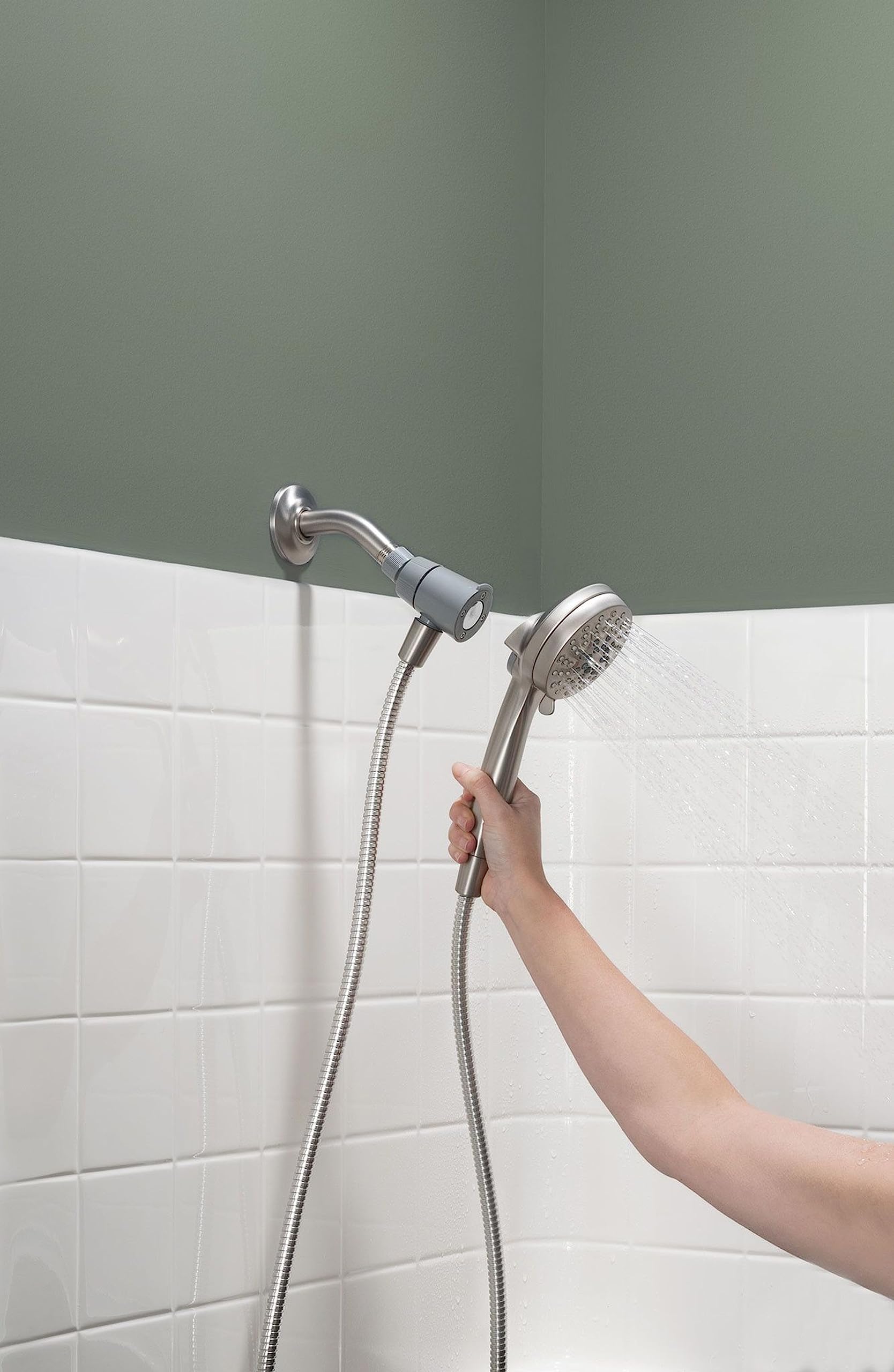 Brushed nickel hand shower with flexible hose mounted on bathroom wall tile, dispensing water spray.