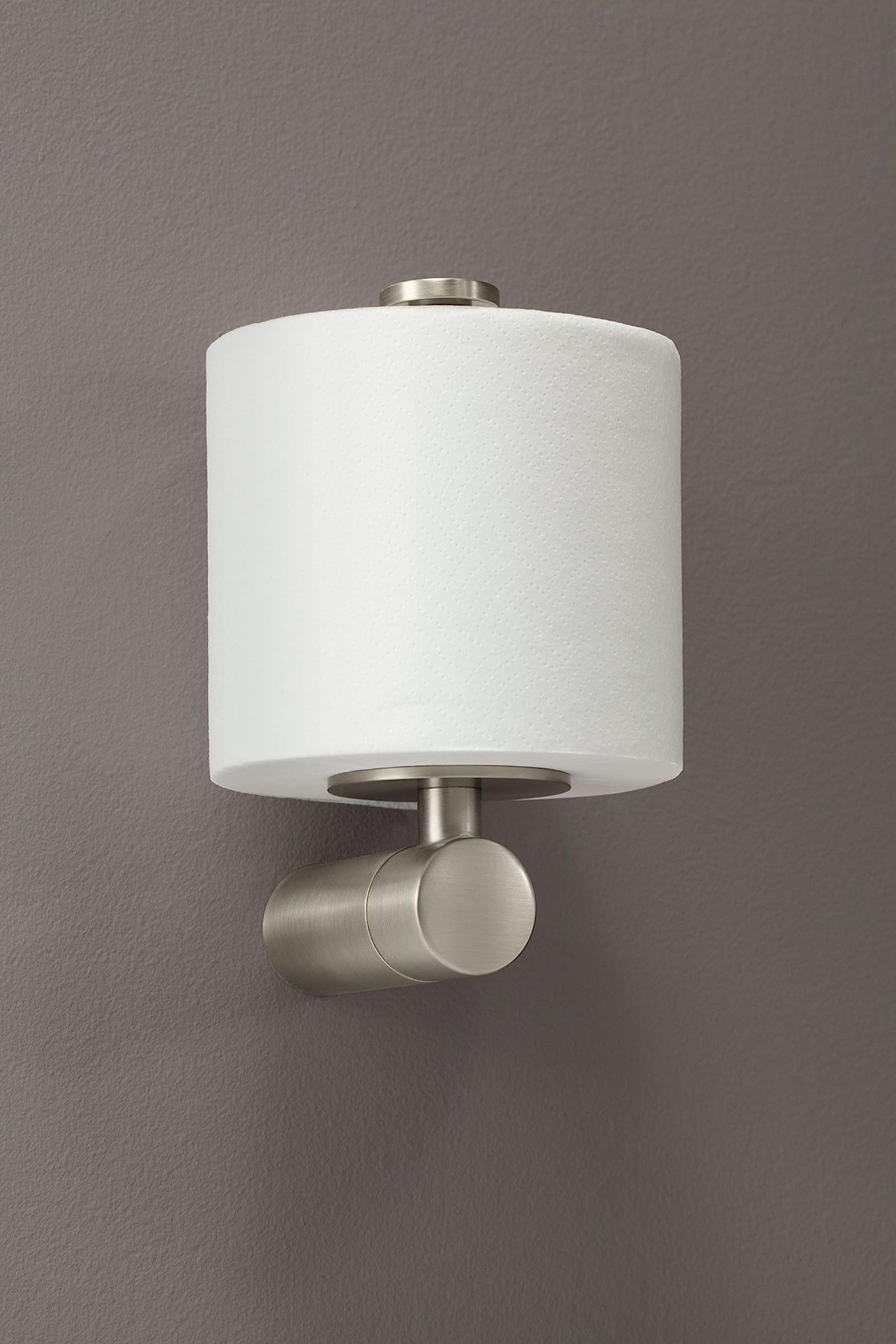 Brushed nickel toilet paper holder with cylindrical white roll and round knob finial mounted on gray wall.
