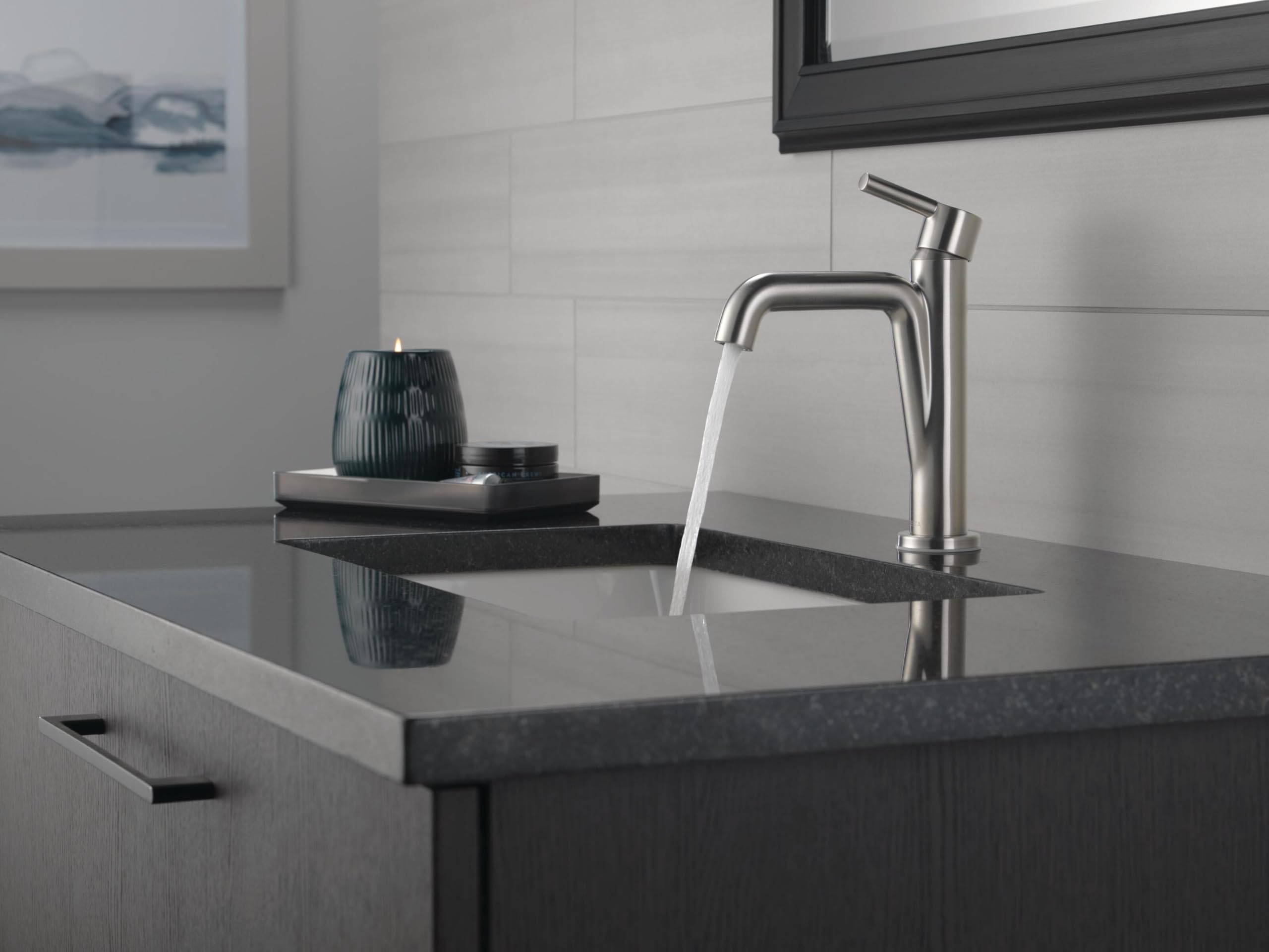 Stainless steel single-handle bathroom faucet with curved spout mounted on dark countertop with water running.