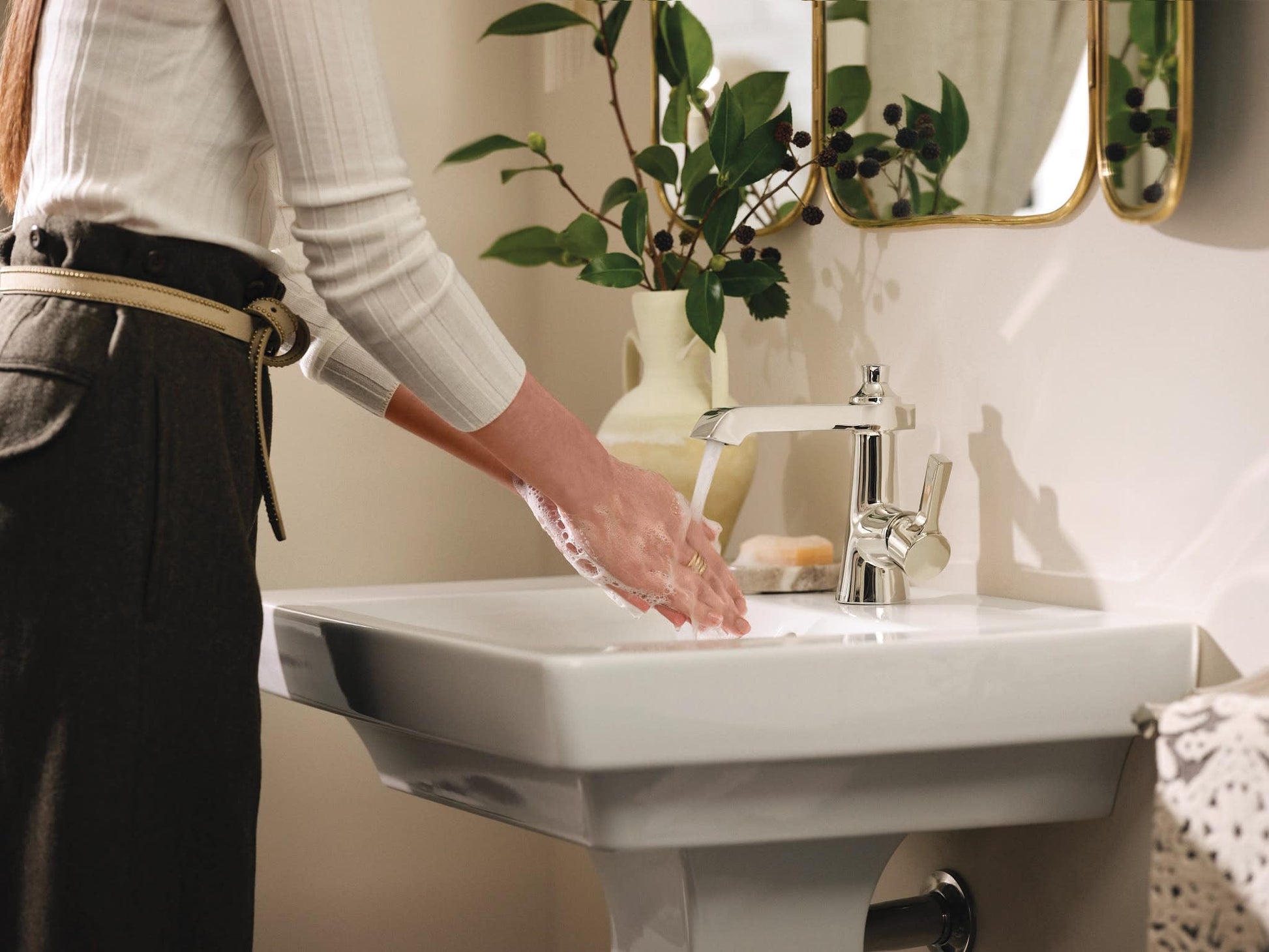 Polished nickel single-handle bathroom faucet with wave touchless activation over white pedestal sink.
