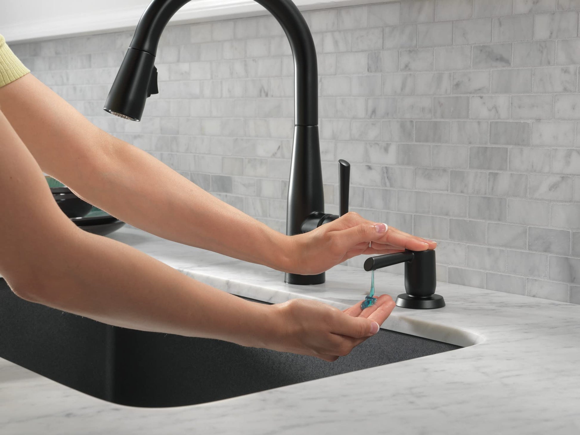 Matte black metal soap dispenser with pump mechanism next to kitchen faucet on countertop.