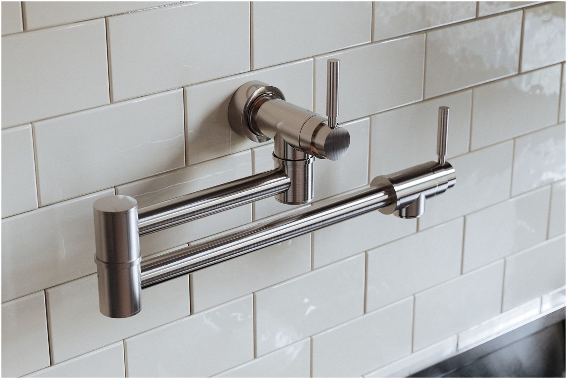 Satin nickel wall-mounted pot filler with dual articulating arms and valve handle installed on white subway tile backsplash.