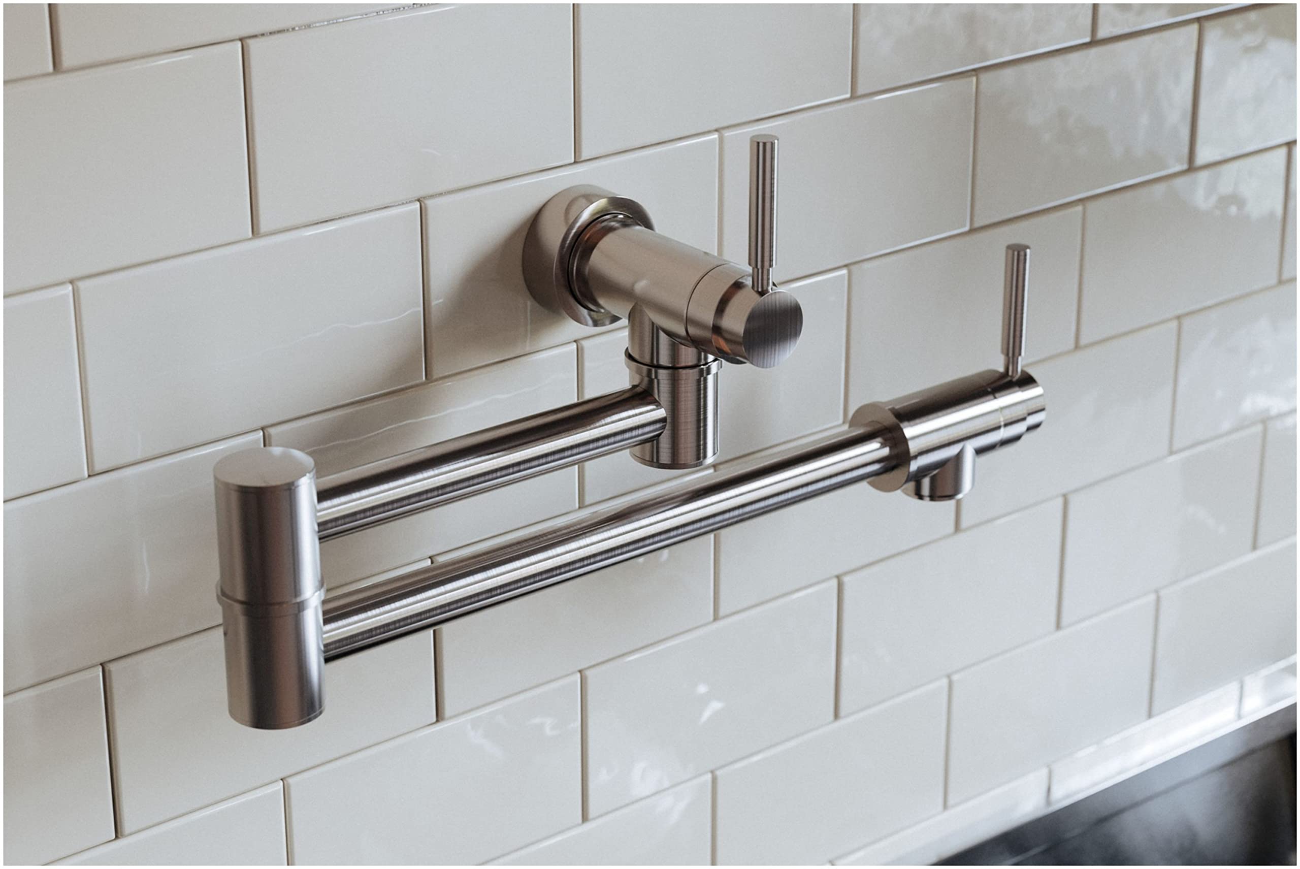 Satin nickel wall-mounted pot filler with dual articulating arms and valve handle installed on white subway tile backsplash.