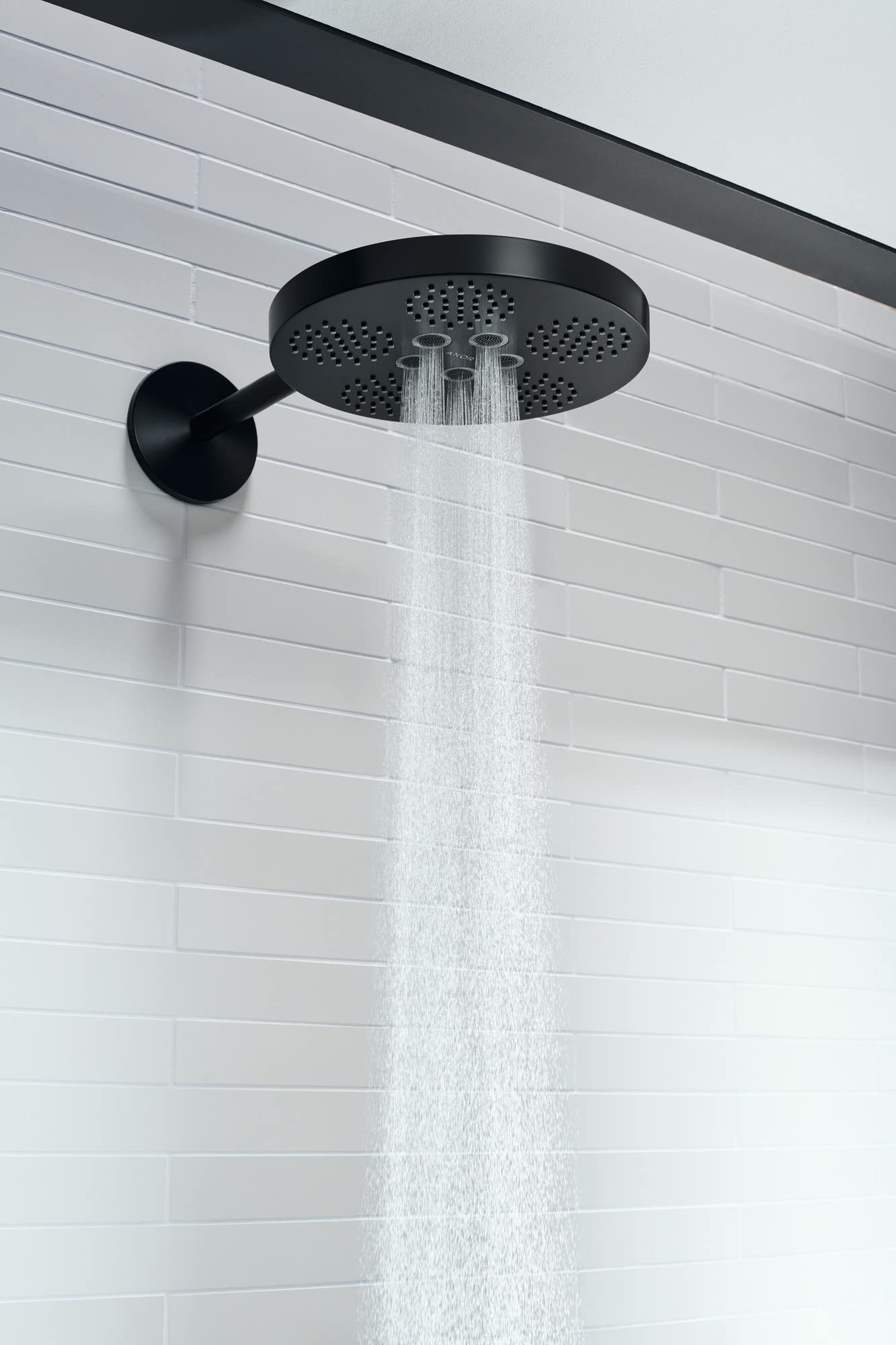 Matte black circular shower head mounted on wall with arm trim, discharging two water jets against white subway tile.
