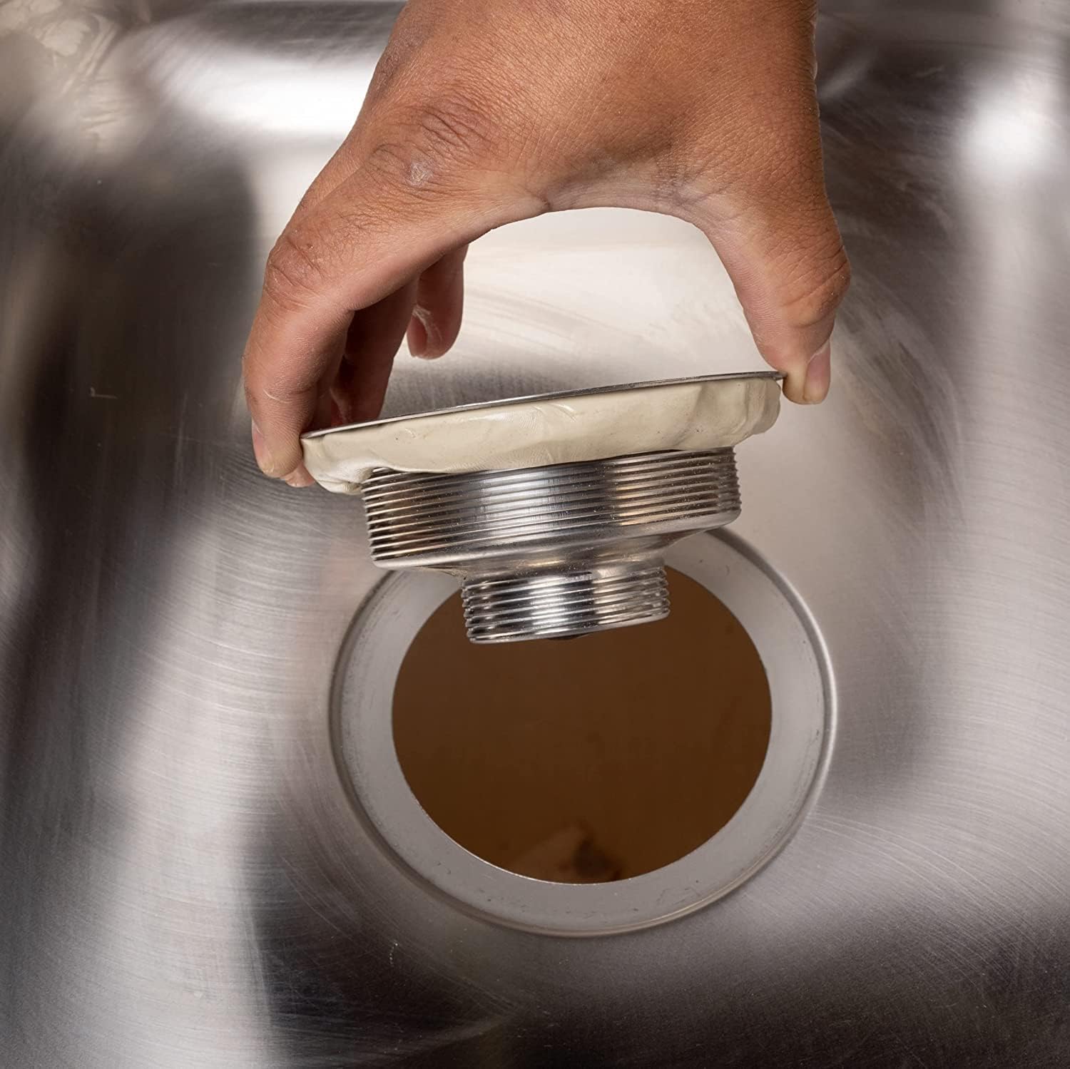Hand holding open container of tan plumber's putty with threaded metal fitting inside.