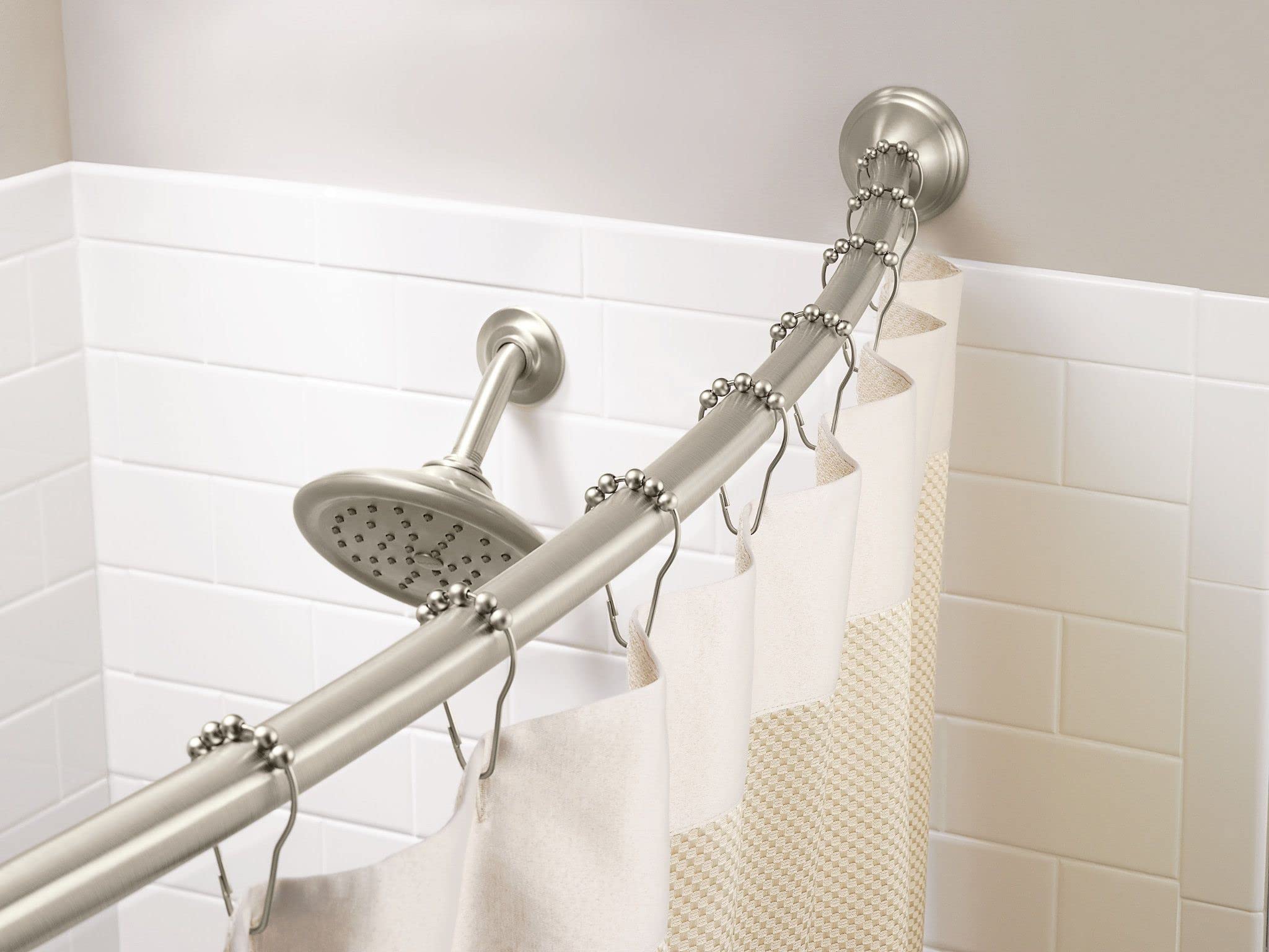 Brushed nickel curved shower rod mounted to white tile wall with matching showerhead and metal rings holding white and tan sh