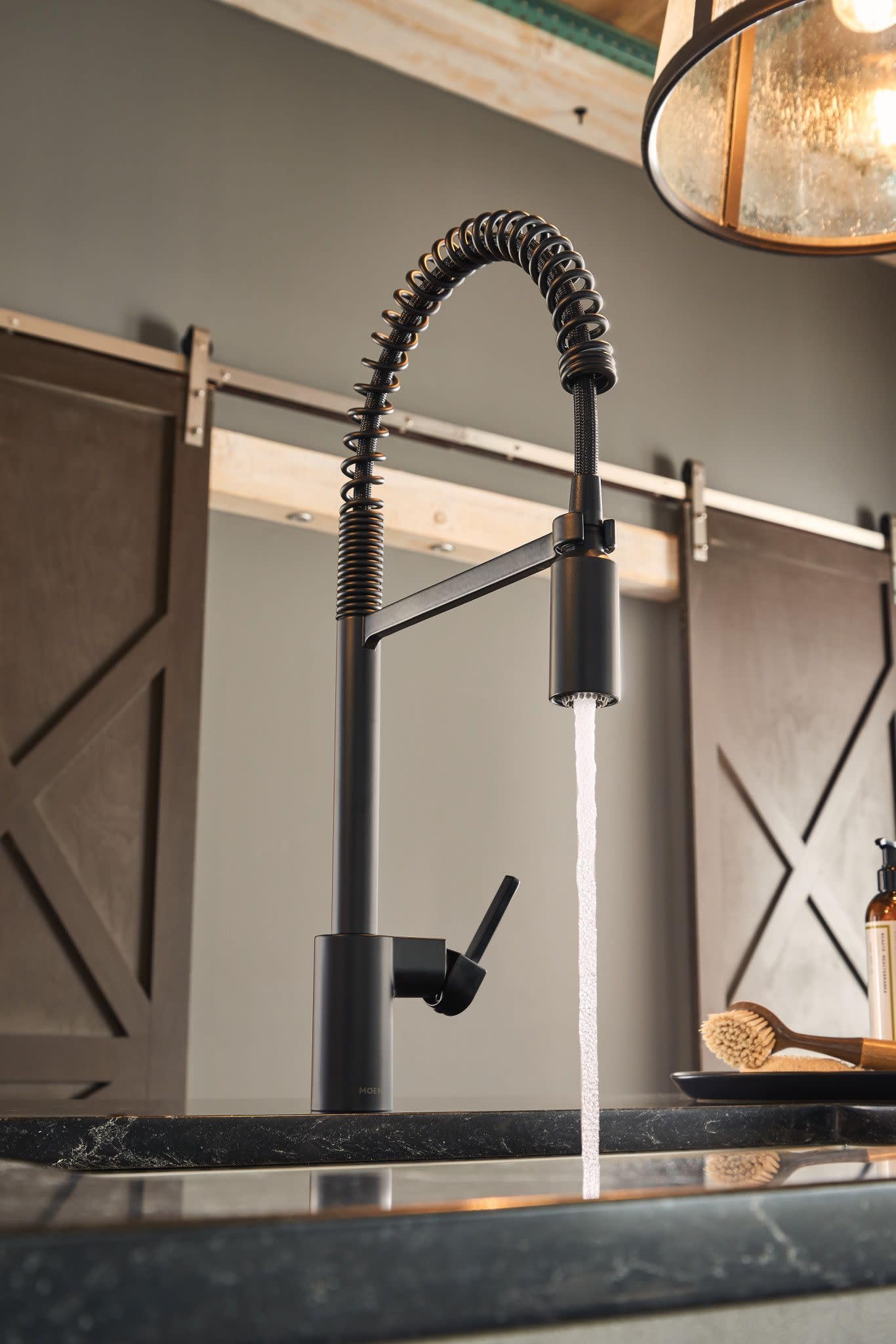 Matte black pulldown kitchen faucet with coiled spring hose and side sprayer handle mounted on dark countertop.
