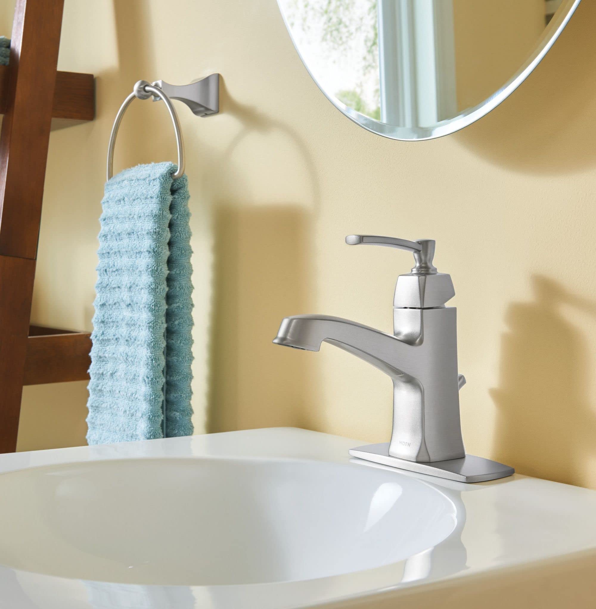 Brushed nickel wall-mounted towel ring holding a folded light blue towel above a bathroom sink.