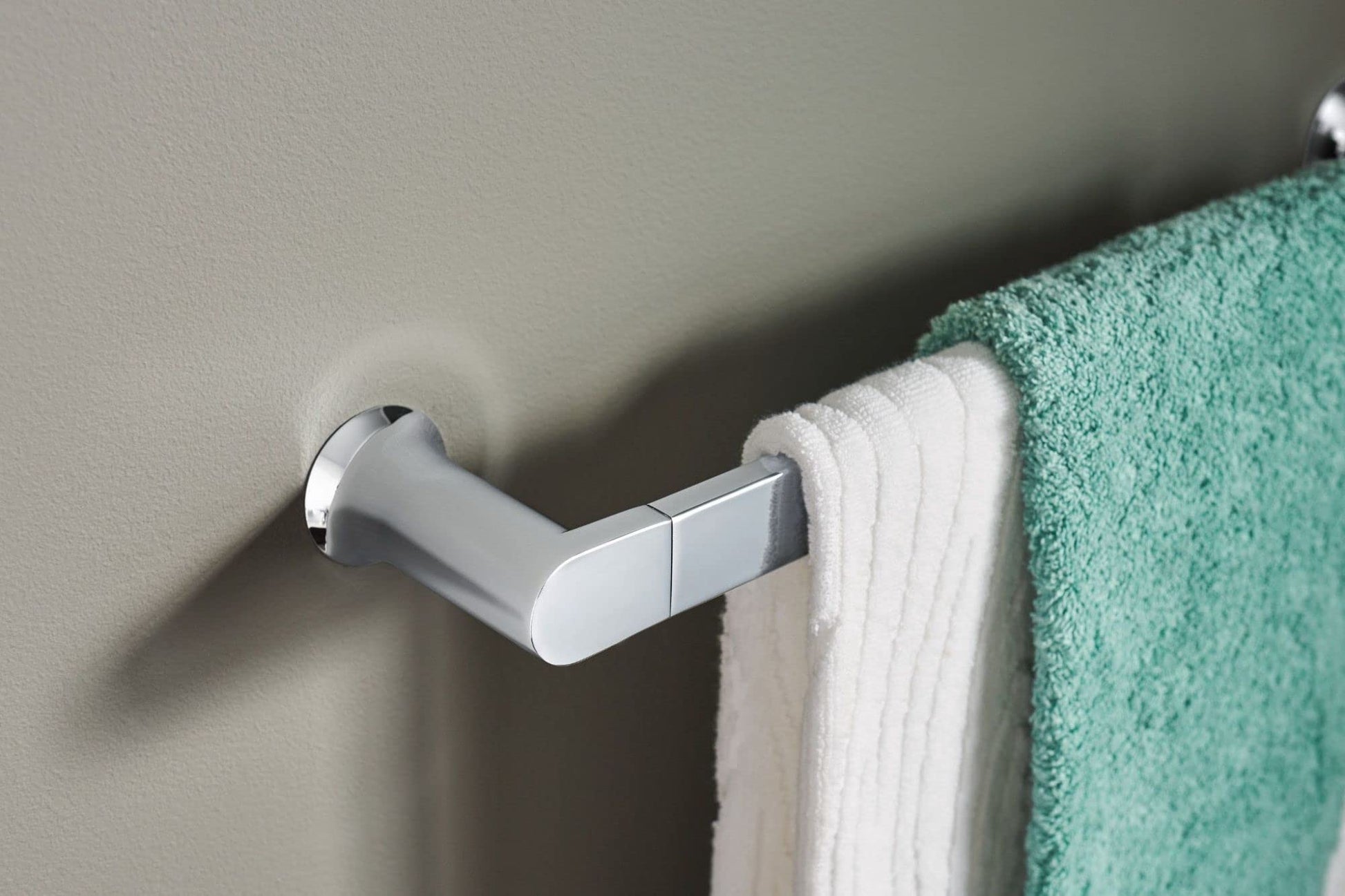 Chrome towel bar mounted on wall with white and green towels draped over it.