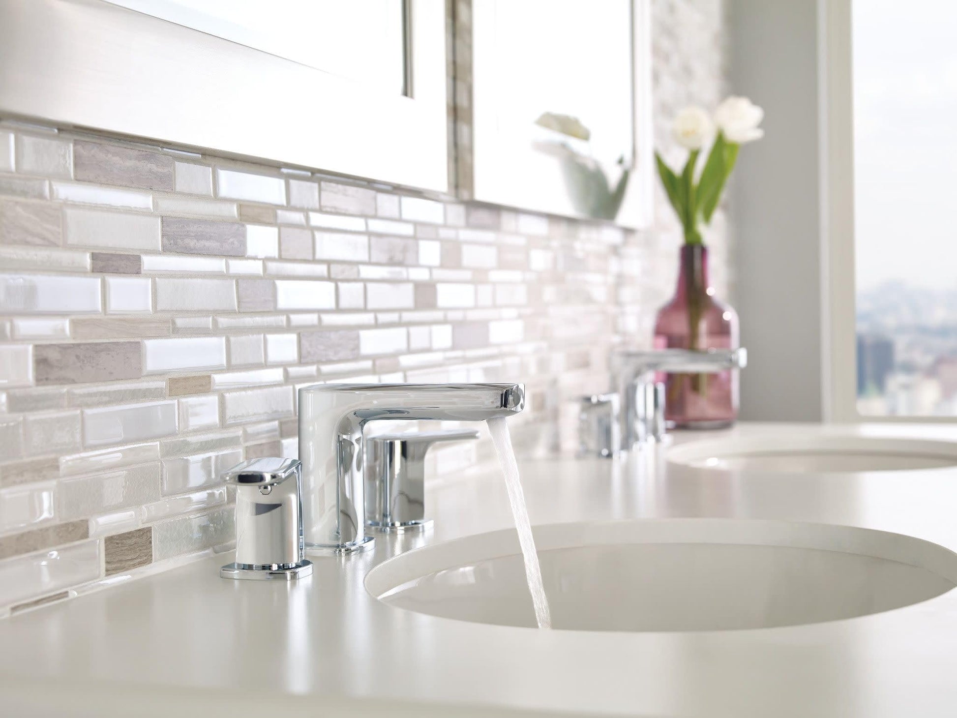 Chrome two-handle widespread bathroom faucet with arcing spout installed on white countertop sink.