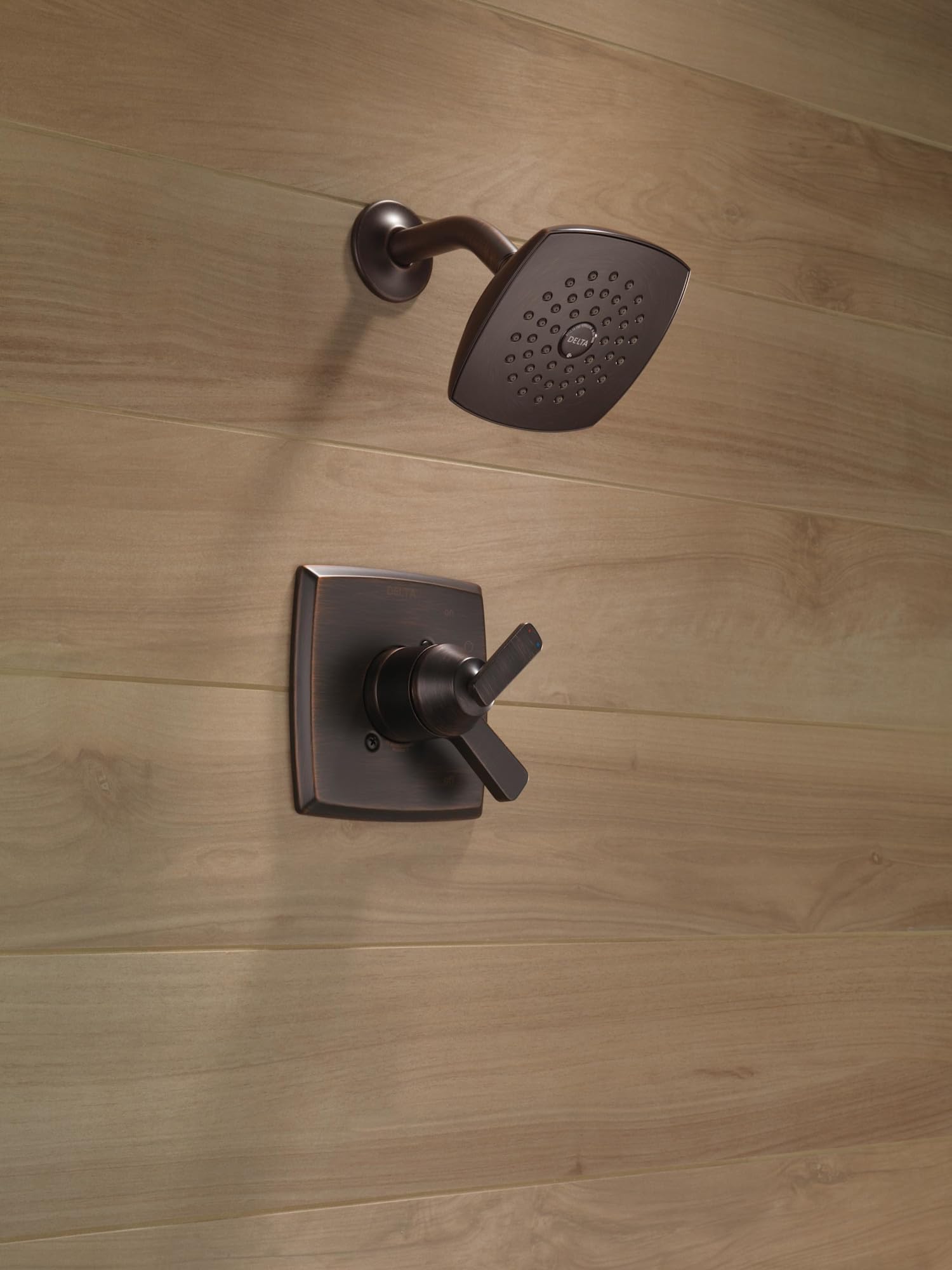 Oil-rubbed bronze shower trim with square showerhead and cross-handle valve mounted on tile wall.