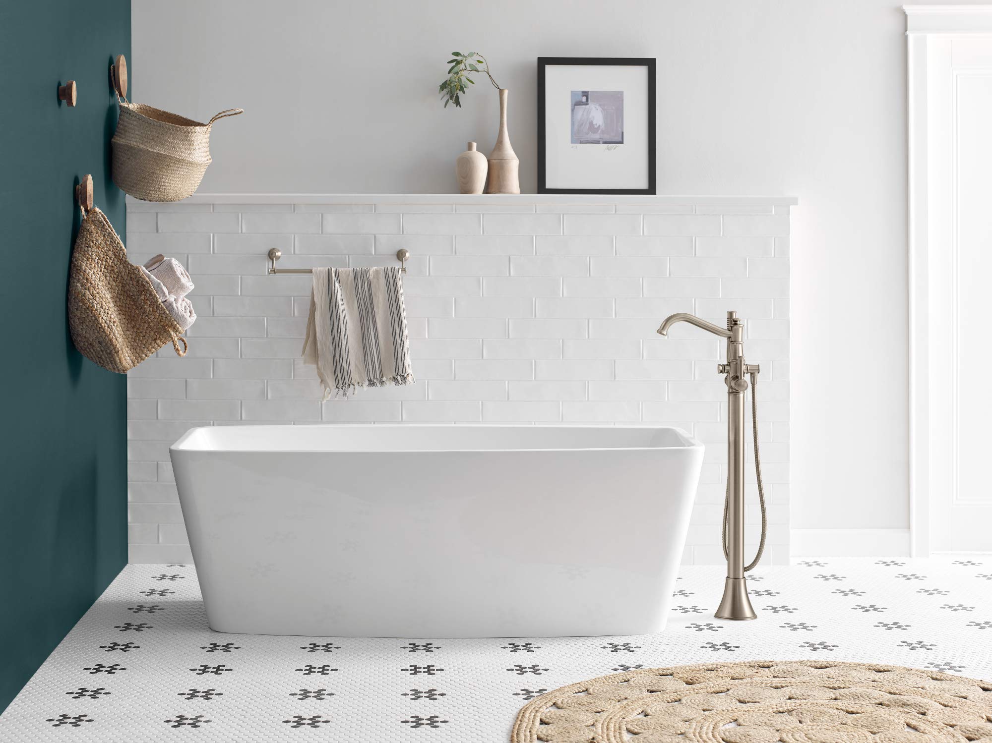 Brushed nickel freestanding floor-mount tub filler with single handle and handheld shower wand next to white soaking tub.