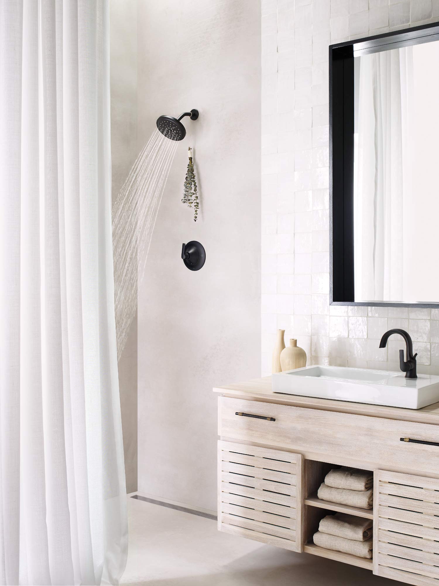 Matte black single-handle shower valve trim with round showerhead and control knob mounted on white tile wall.
