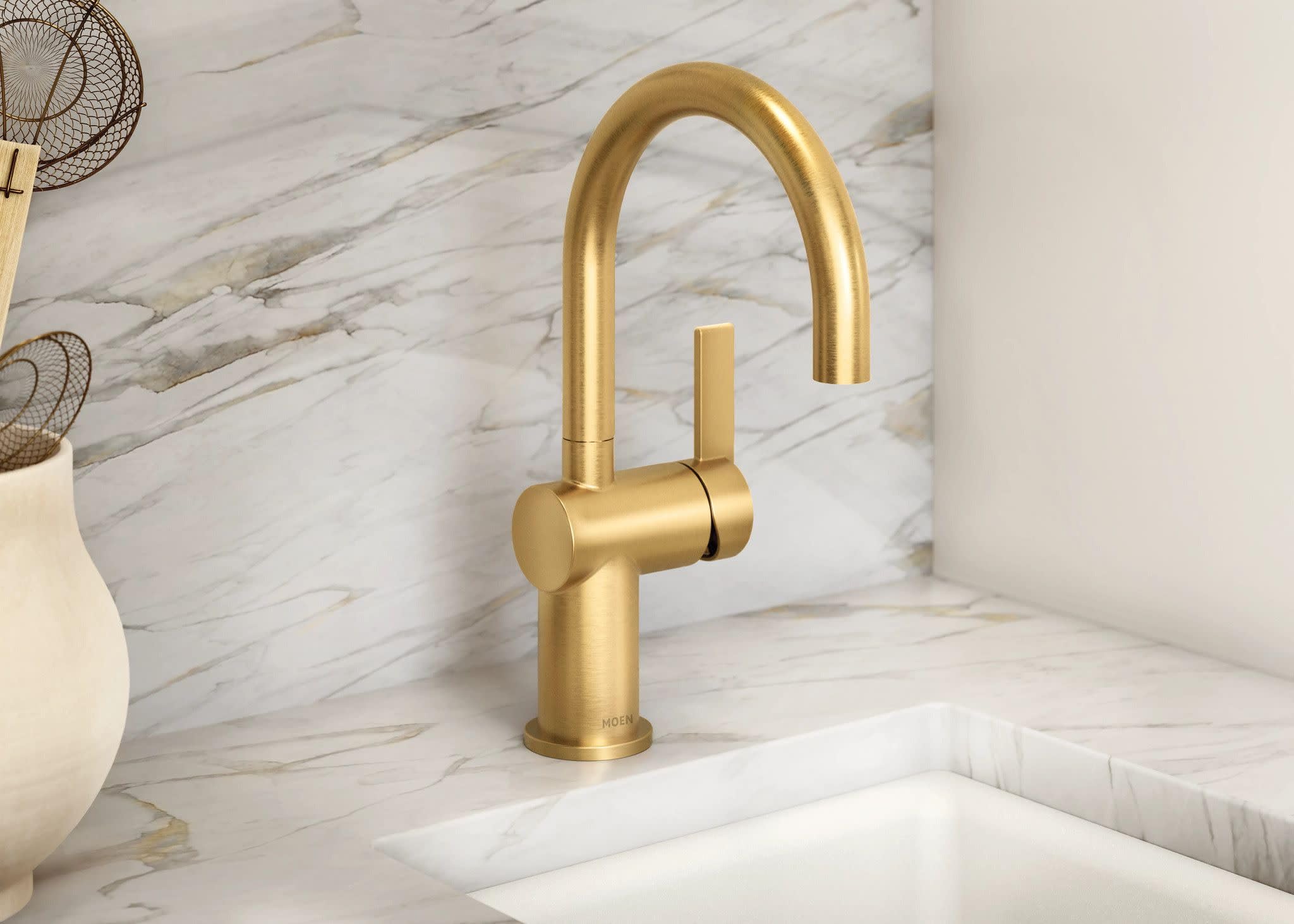 Brushed gold bar faucet with single lever handle and curved spout mounted on marble countertop.