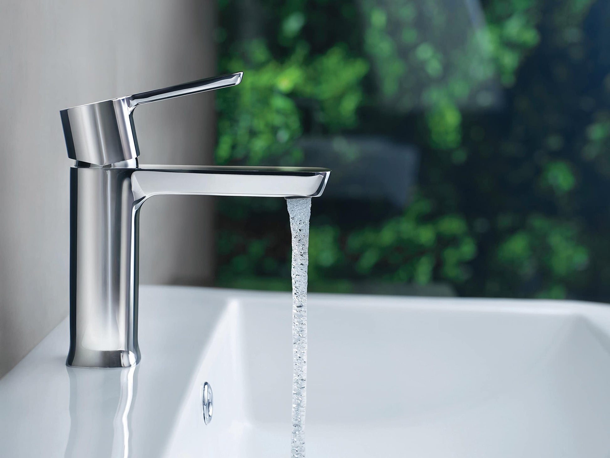 Chrome single-handle bathroom faucet with cylindrical body and angled spout, water flowing into white sink.