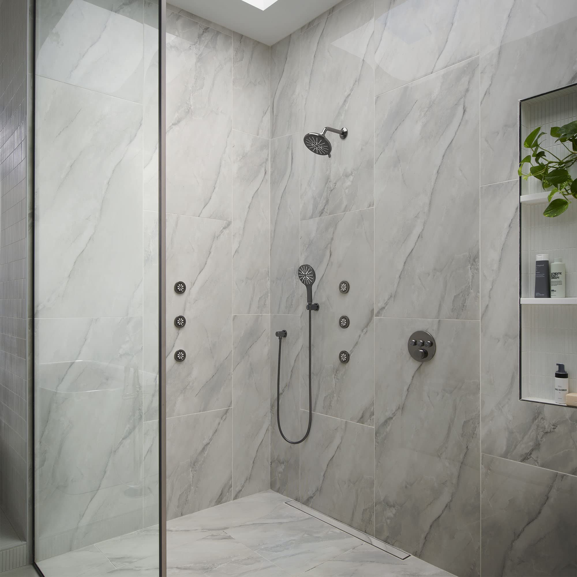 Dark graphite curved shower arm mounted on marble tile wall above rainfall showerhead.