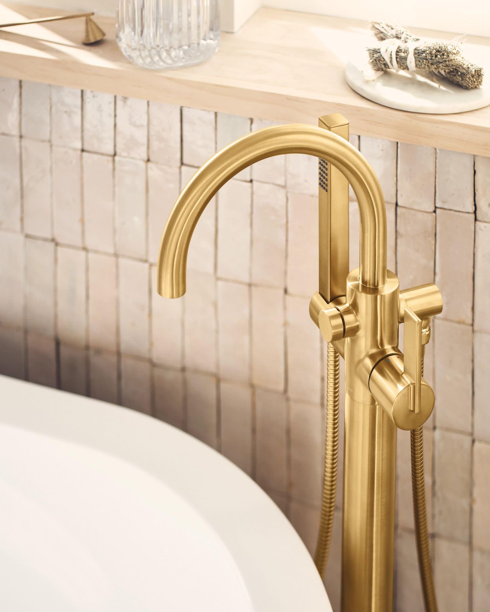 Brushed gold freestanding tub filler with curved spout, single handle, and detachable handshower on hose.