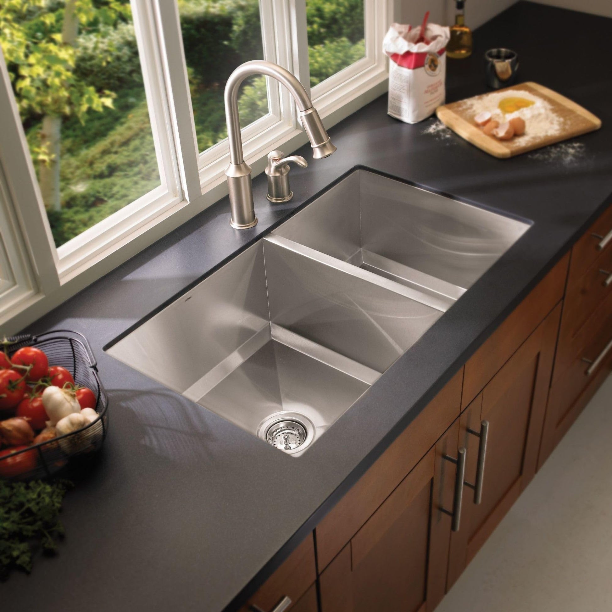 Stainless steel double bowl undermount kitchen sink installed in black countertop with faucet.