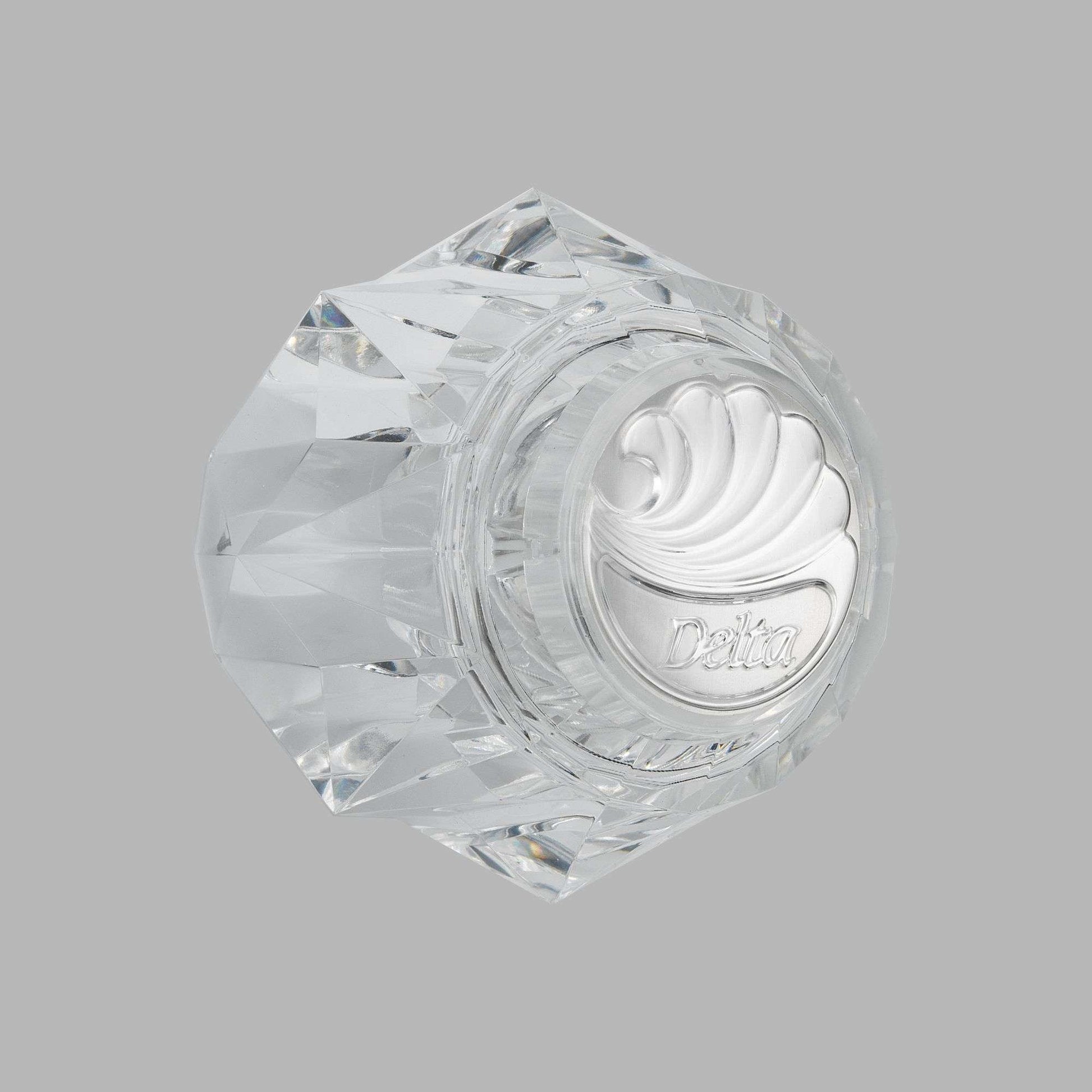 Clear acrylic hexagonal knob handle with Delta branding and decorative swirl pattern on face.
