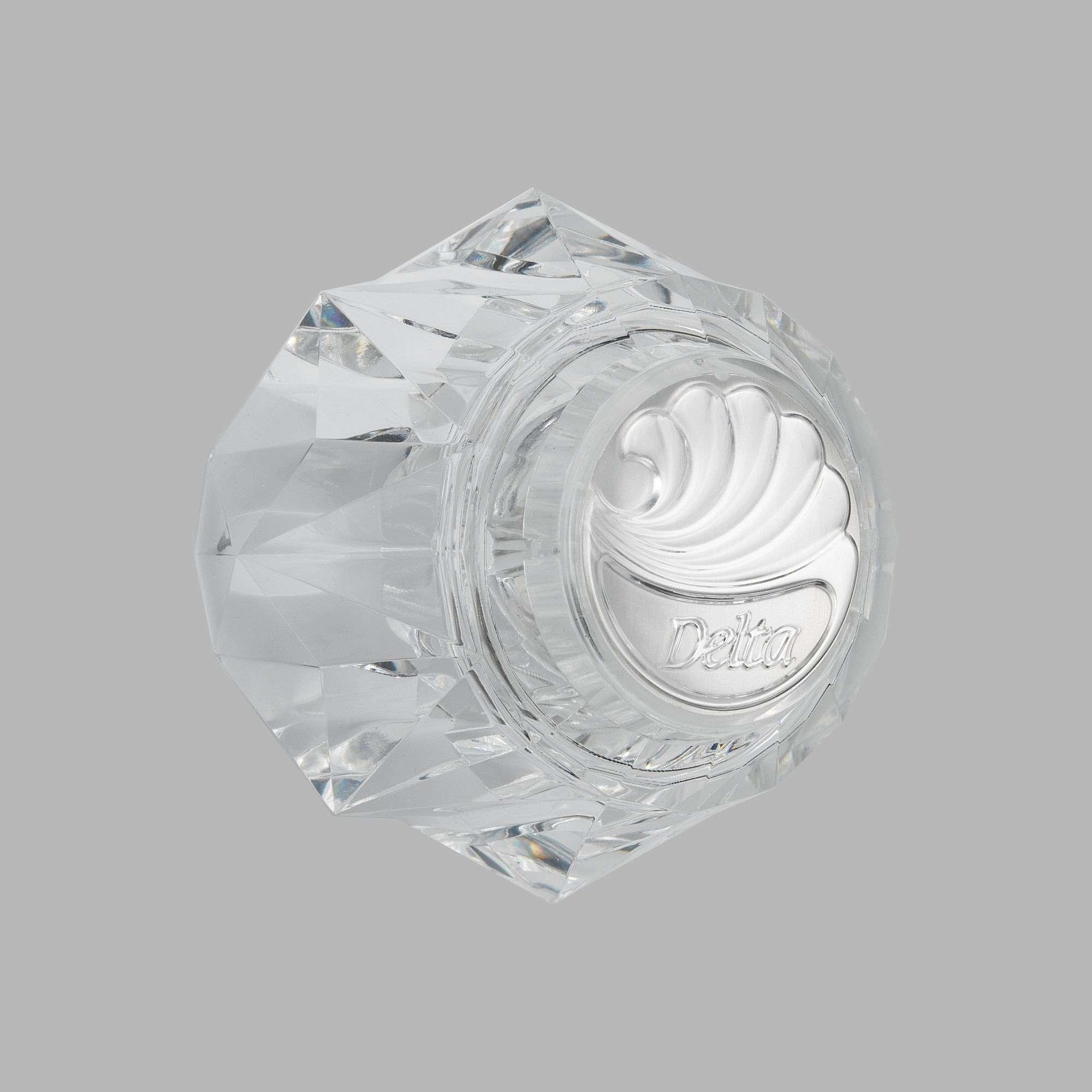 Clear acrylic hexagonal knob handle with Delta branding and decorative swirl pattern on face.
