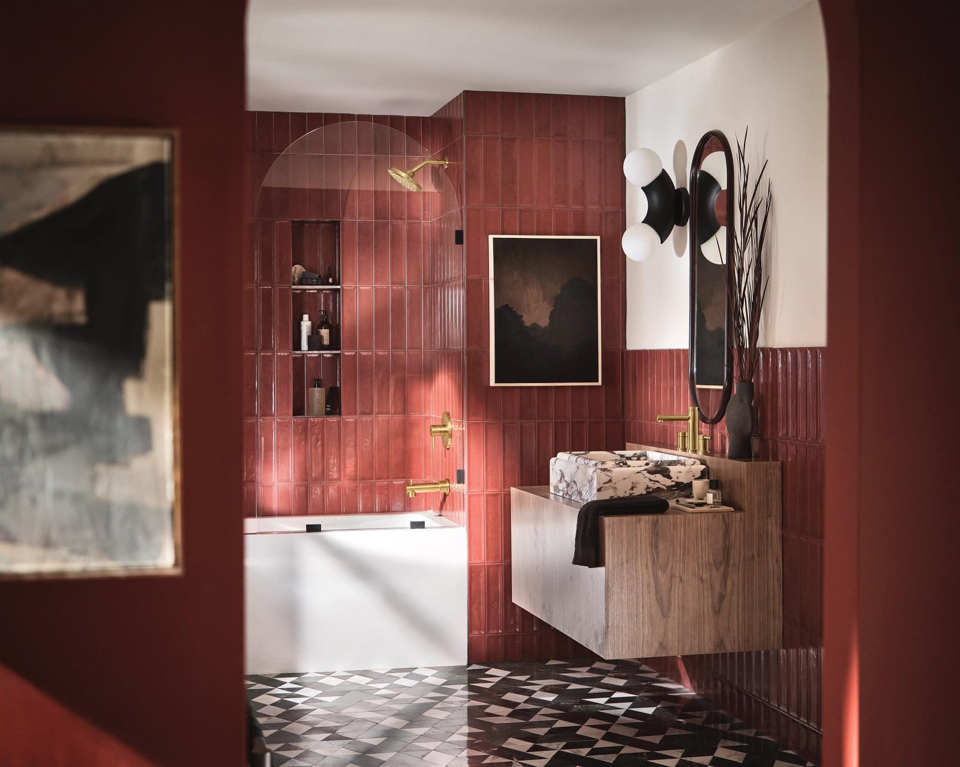 Brushed gold single-handle tub and shower trim kit installed in red tile shower enclosure with glass door.