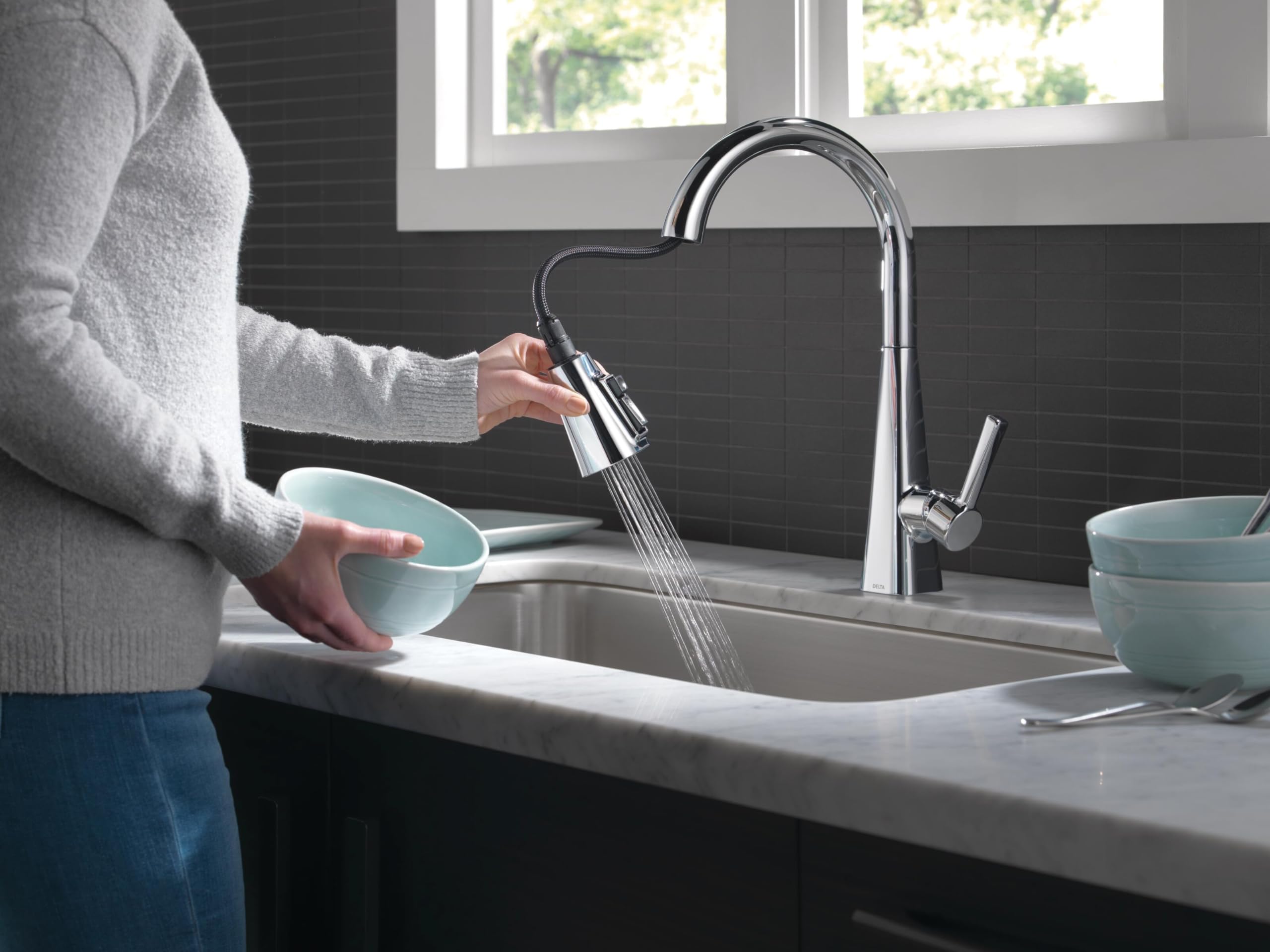 Chrome single-handle pull-down kitchen faucet with spray nozzle extended over sink.