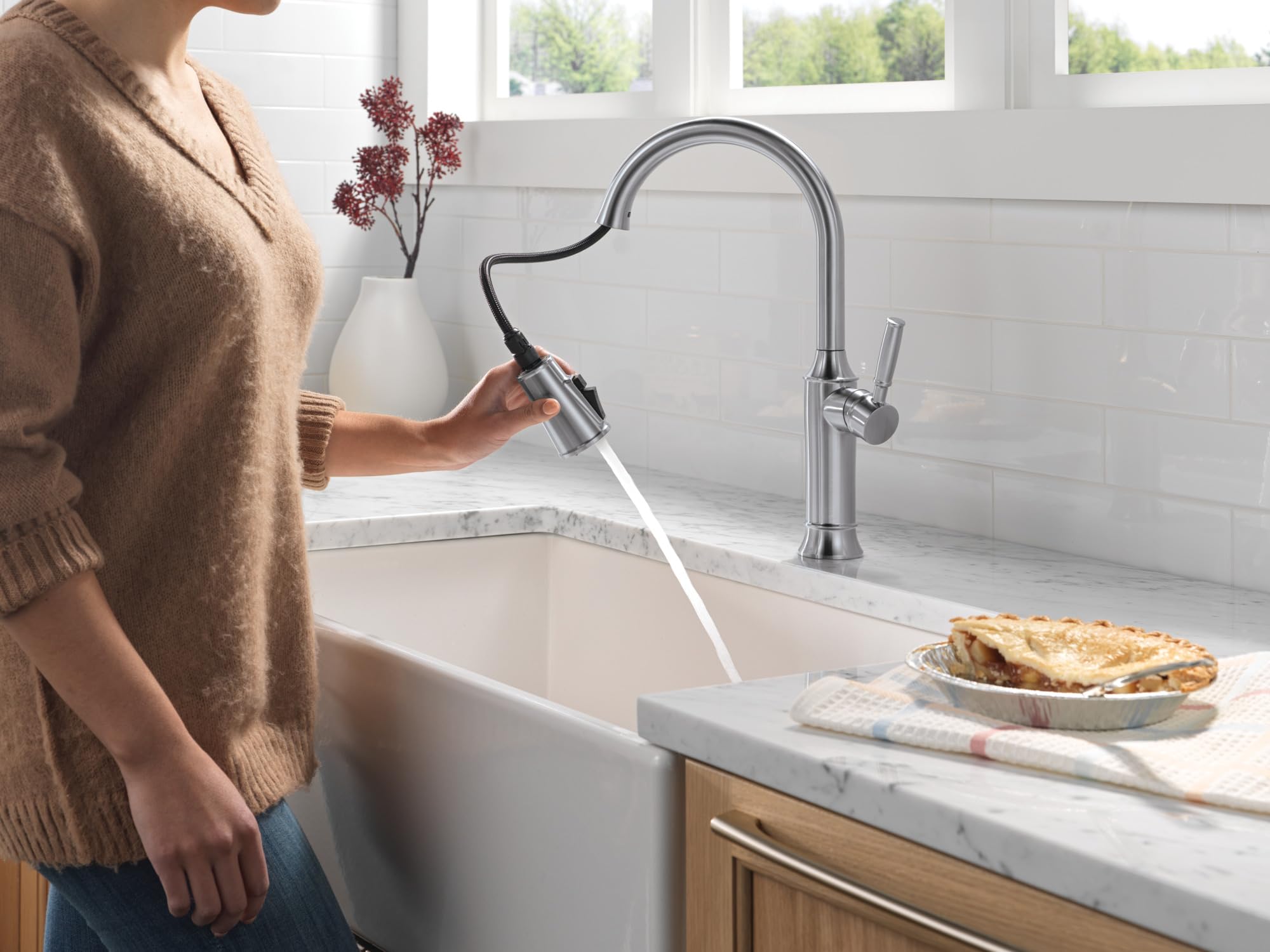 Stainless steel pull-down kitchen faucet with curved spout and single handle, shown in use over white sink.
