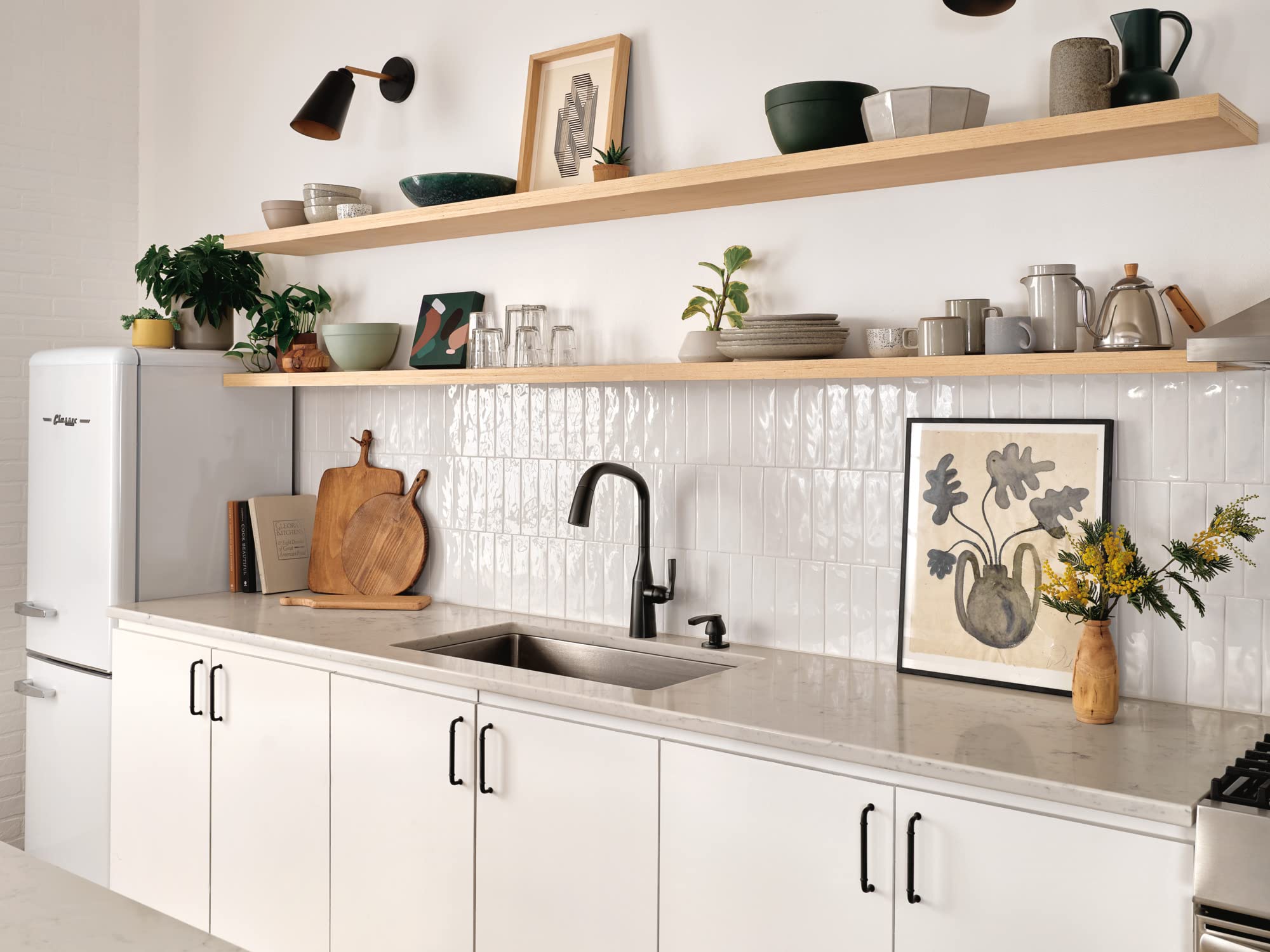 Matte black soap and lotion dispenser mounted on white subway tile backsplash next to kitchen sink faucet.
