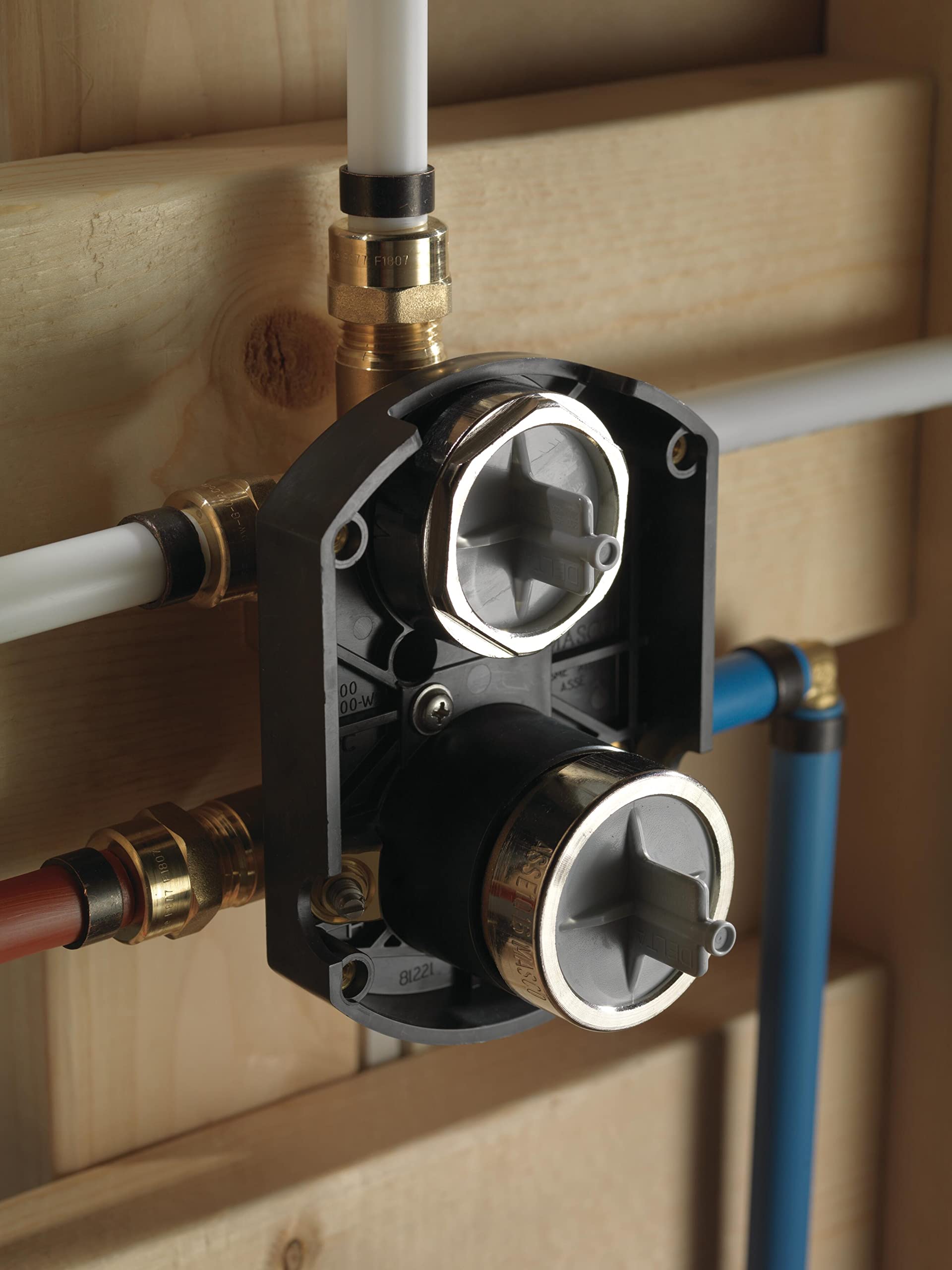 Black integrated shower diverter rough-in valve with dual white handles and brass threaded connections mounted in wood framin