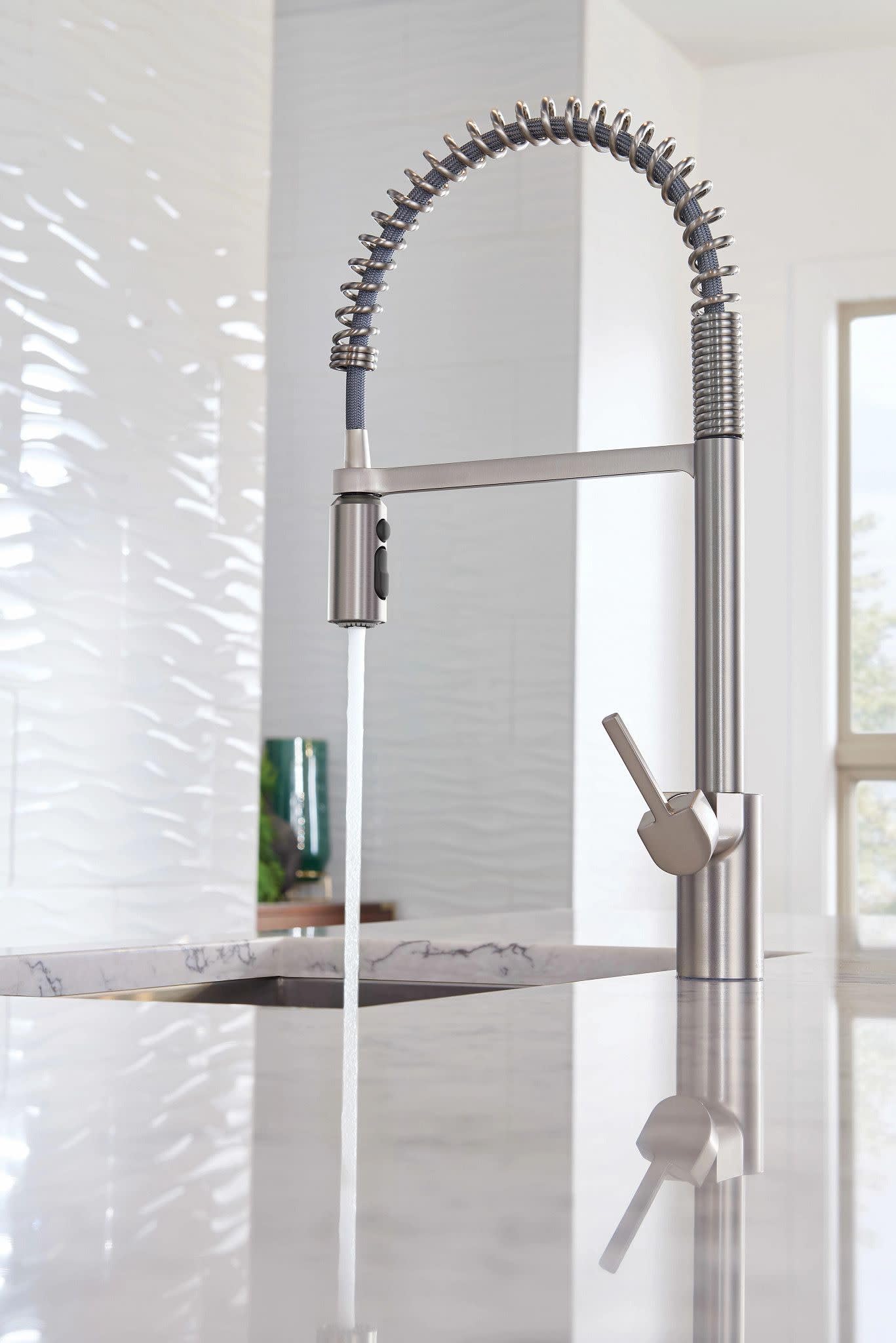 Stainless steel kitchen faucet with coiled spring pull-down spout and dual handles mounted above sink.