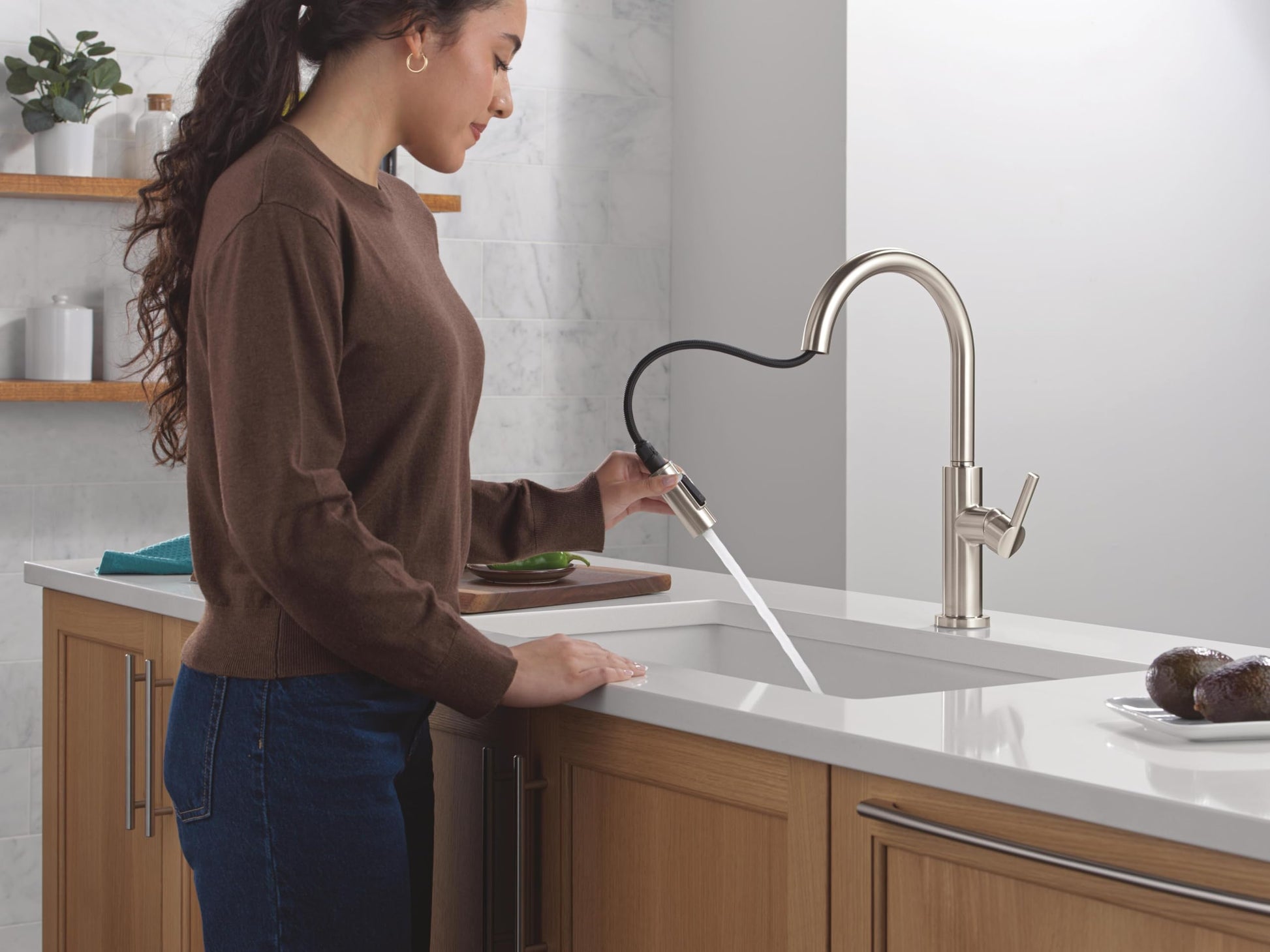 Stainless steel single-handle pull-down kitchen faucet with flexible hose and high arc spout over white sink.