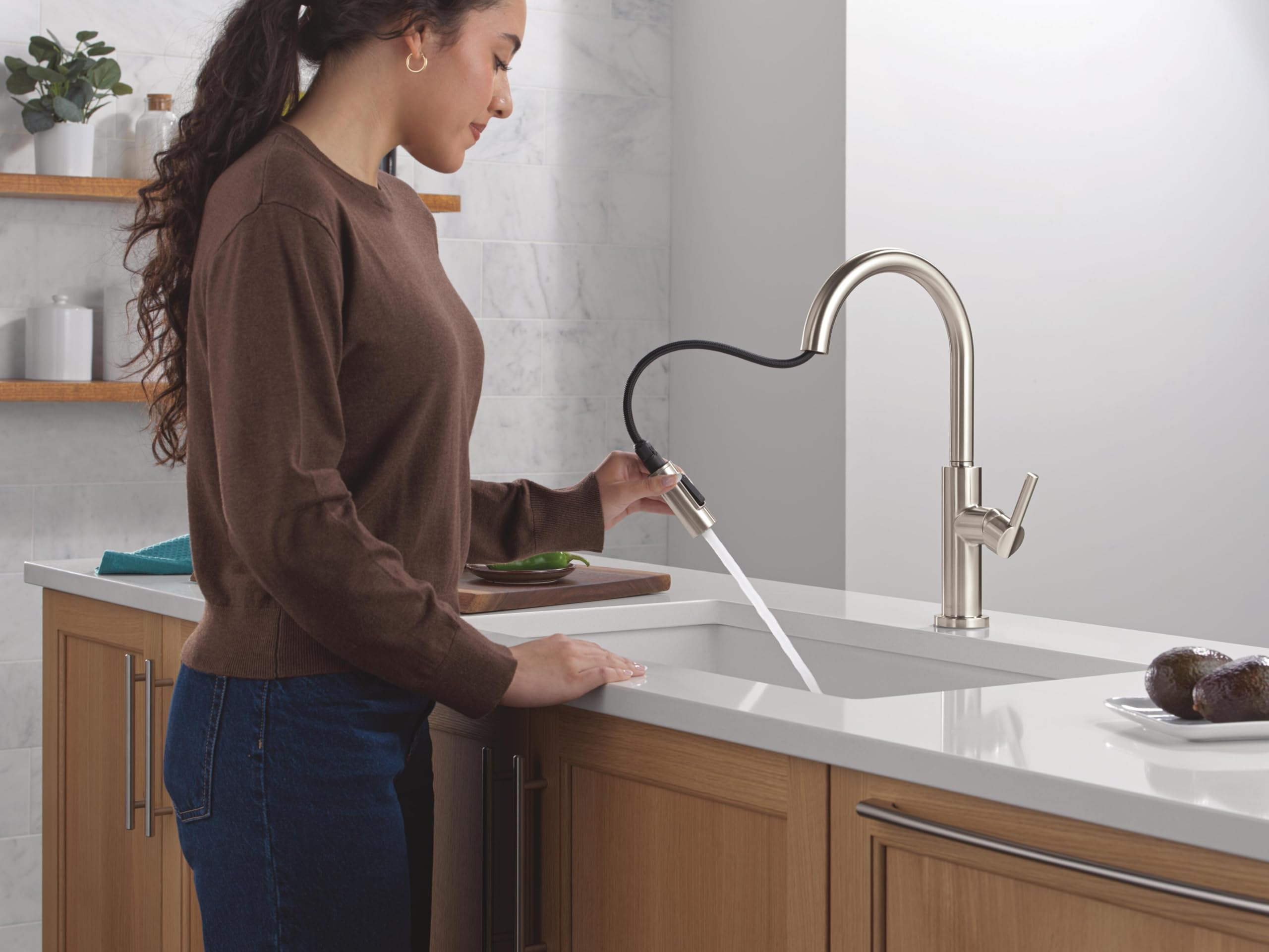 Stainless steel single-handle pull-down kitchen faucet with flexible hose and high arc spout over white sink.