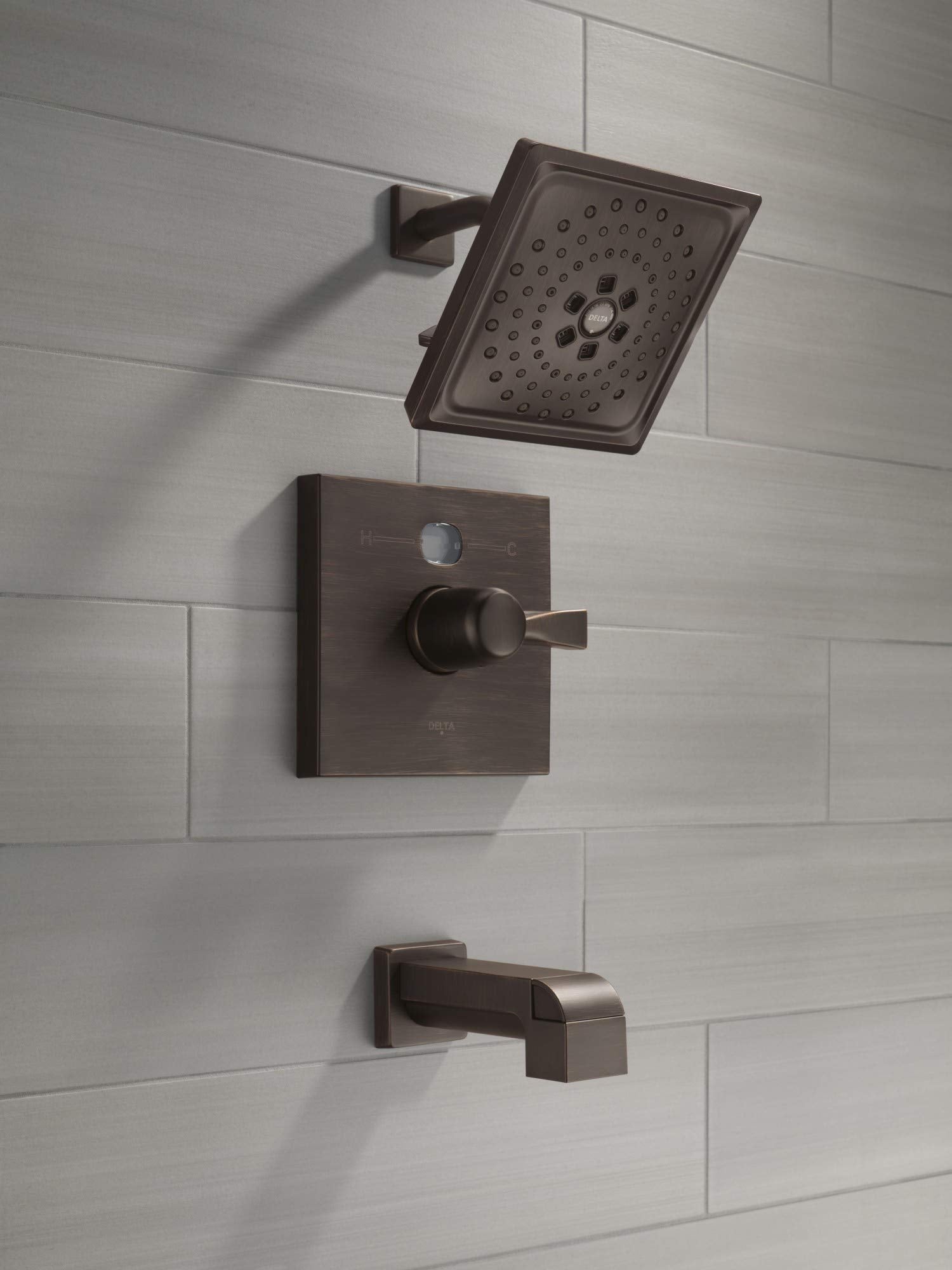 Champagne bronze tub spout with pull-up diverter and matching showerhead and control valve mounted on tile wall.