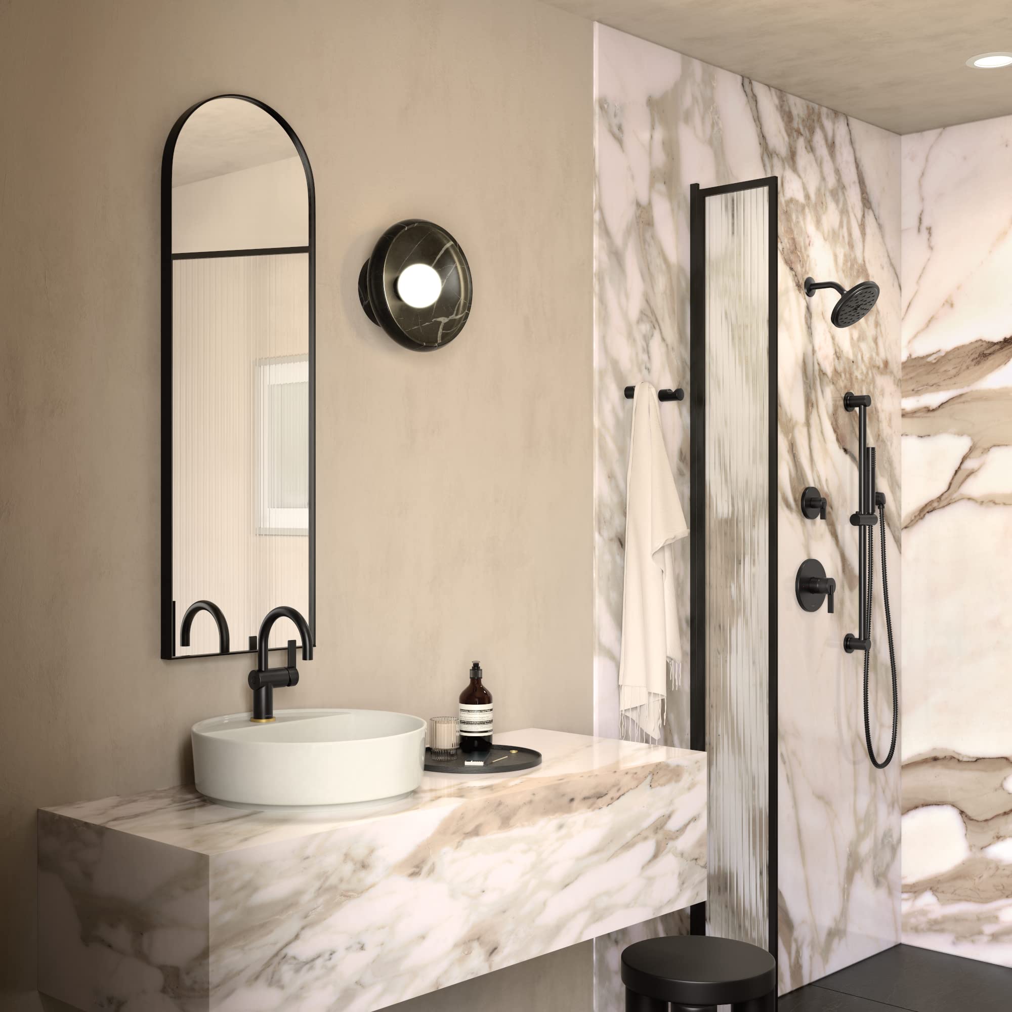 Matte black single-handle faucet trim with circular escutcheon installed above white vessel sink in marble bathroom.