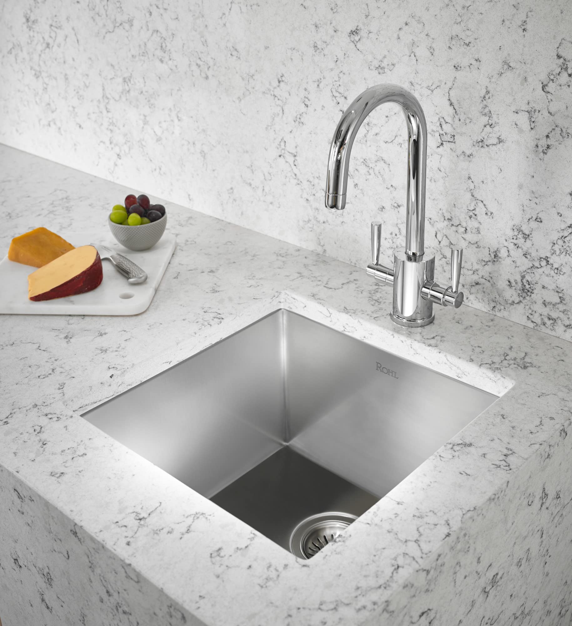 Brushed stainless steel single-bowl undermount sink with arched chrome faucet and side sprayer in marble countertop.