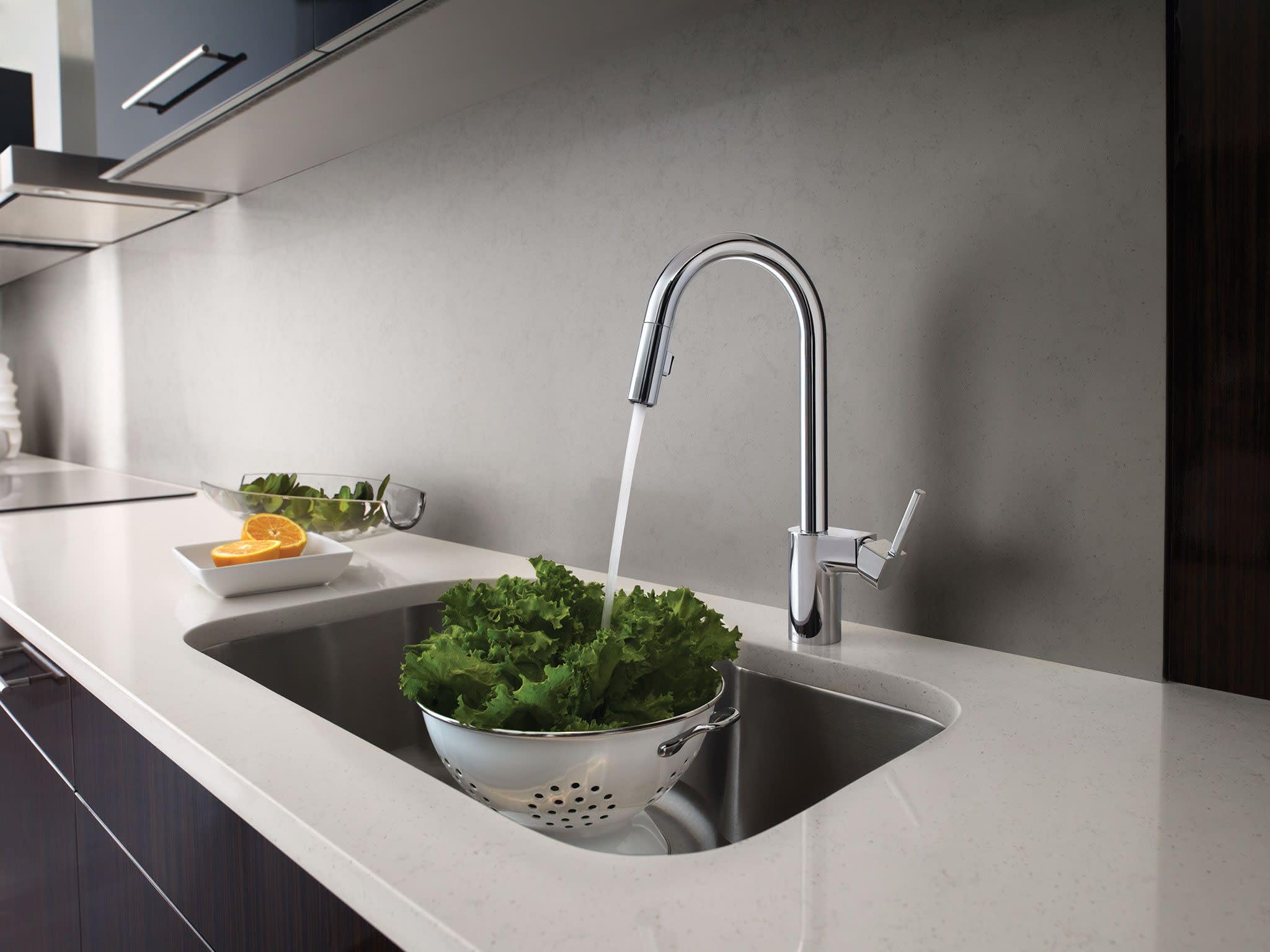 Chrome pulldown kitchen faucet with single handle installed above stainless steel sink in modern kitchen.