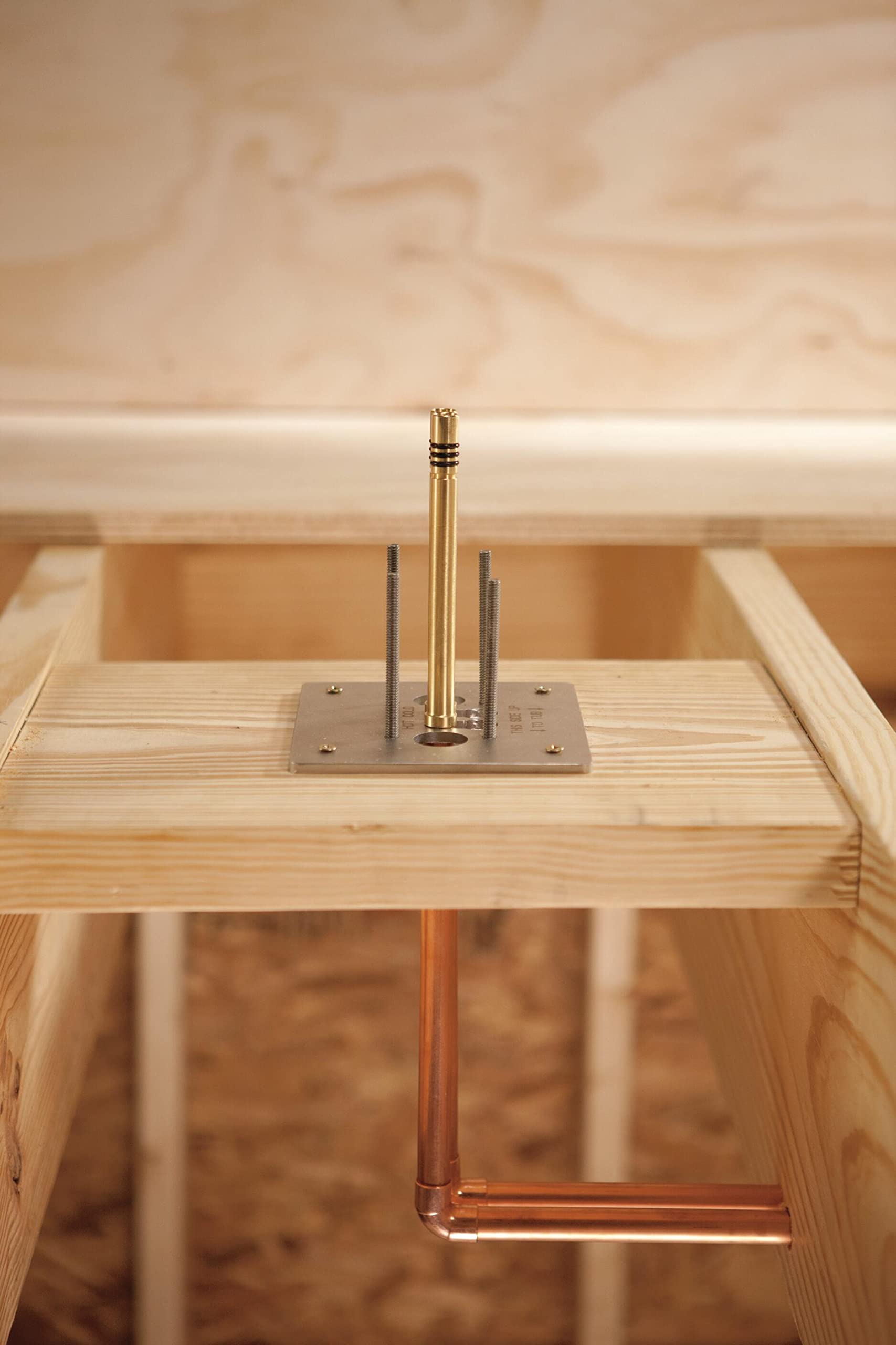 Floor-mounted brass tub filler rough-in with copper supply lines and mounting plate installed in wooden frame.