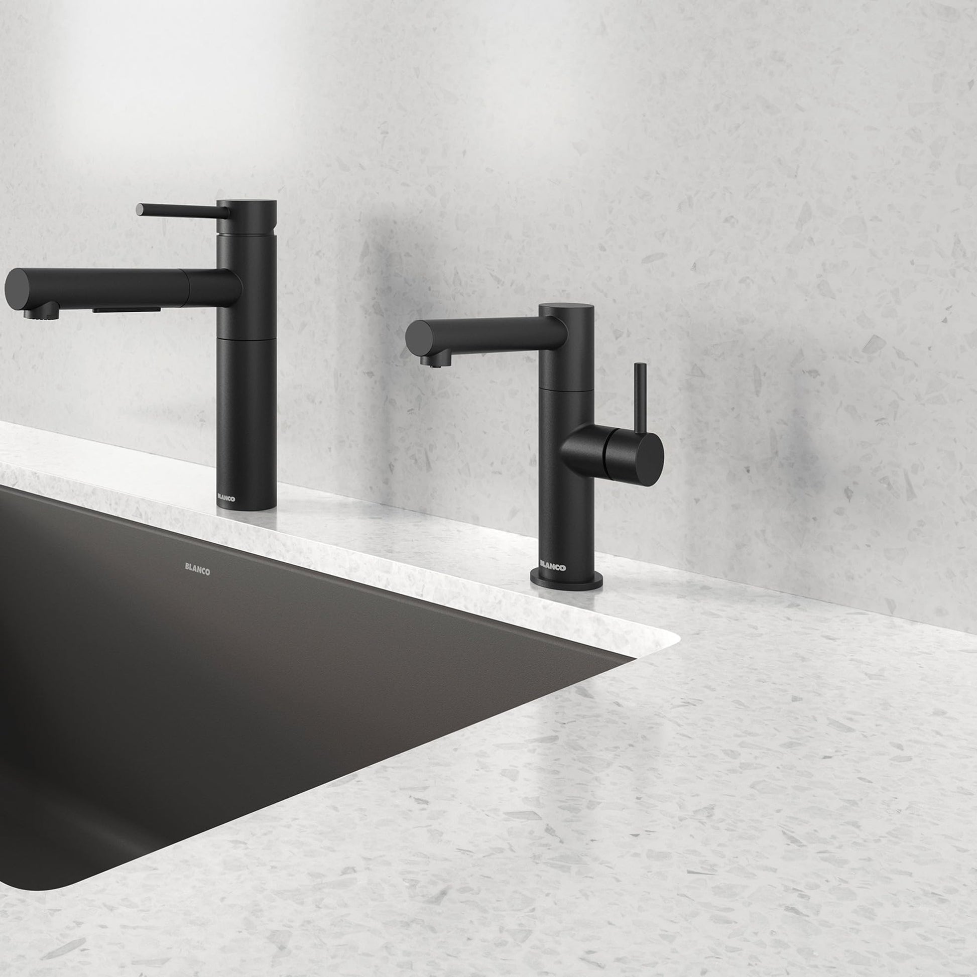 Two matte black single-handle beverage faucets with cylindrical spouts mounted on a marble countertop above a black sink.