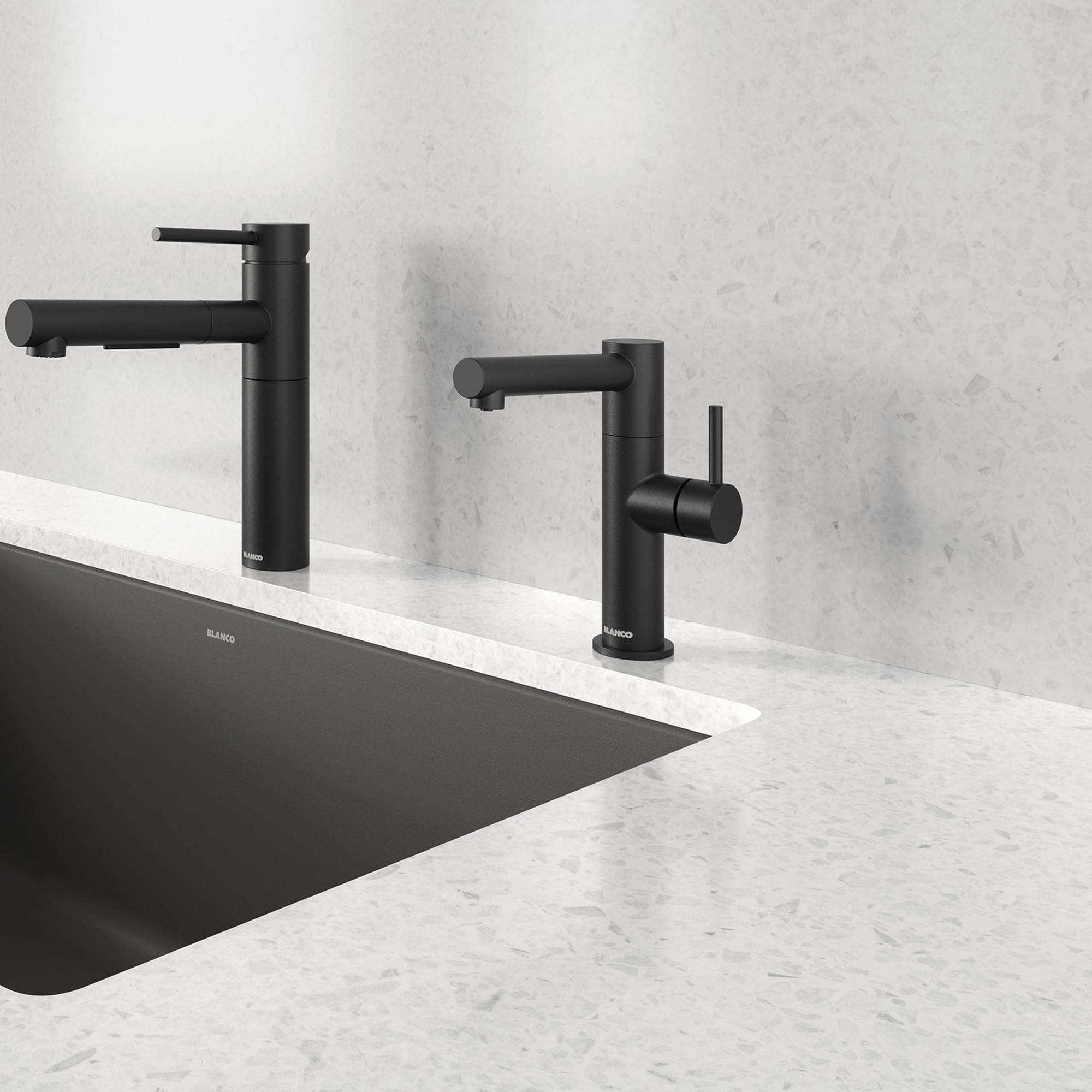 Two matte black single-handle beverage faucets with cylindrical spouts mounted on a marble countertop above a black sink.