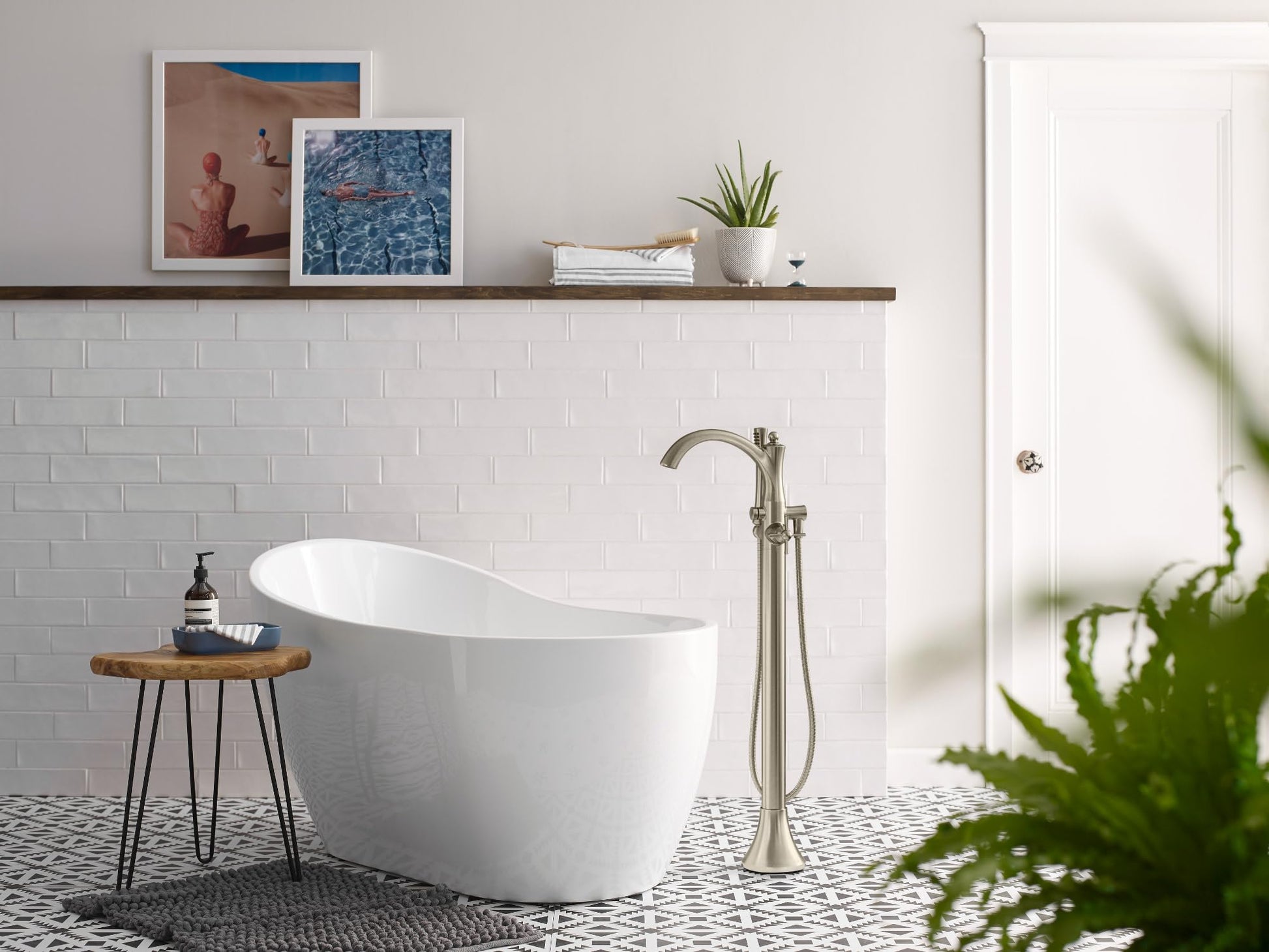 Chrome freestanding tub filler with curved spout and handheld showerhead mounted beside white soaking tub.