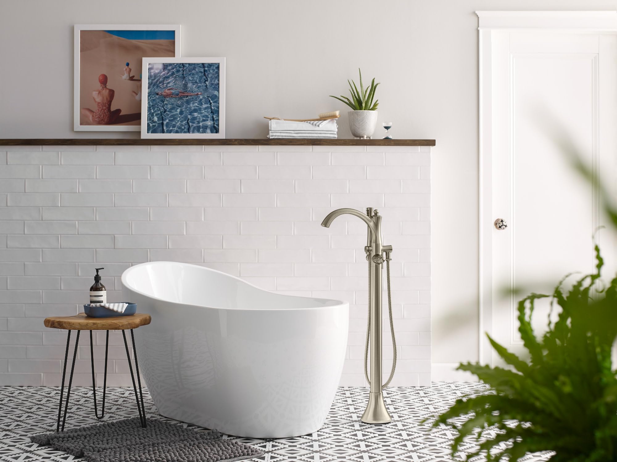 Chrome freestanding tub filler with curved spout and handheld showerhead mounted beside white soaking tub.
