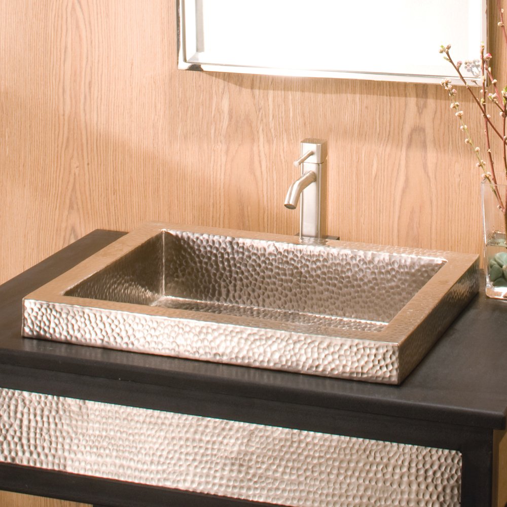 Rectangular hammered copper sink with raised rim on black countertop with chrome faucet.
